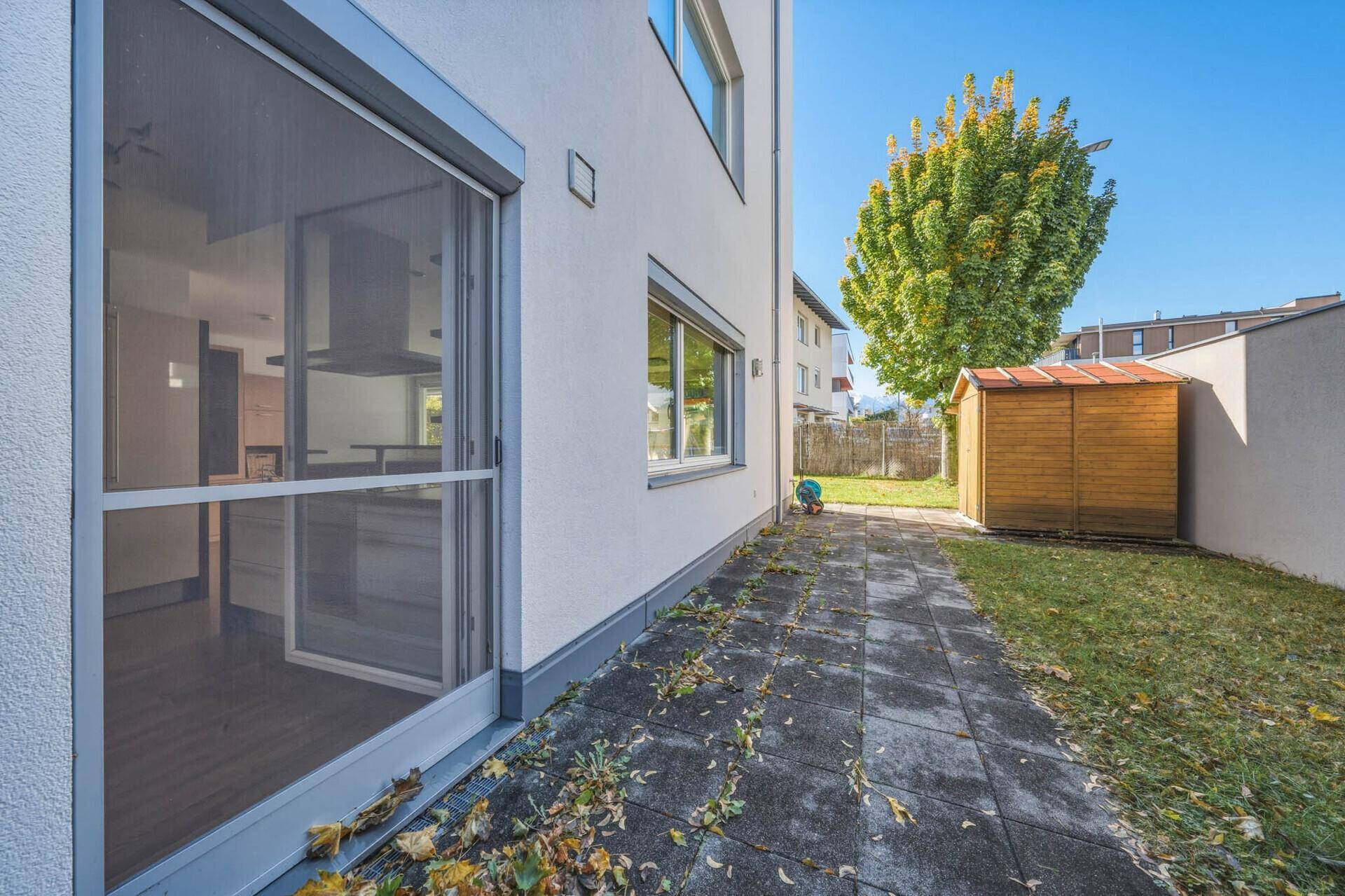 Kleiner Gartenbereich mit gepflastertem Weg, Rasenfläche und einem Gartenhaus.