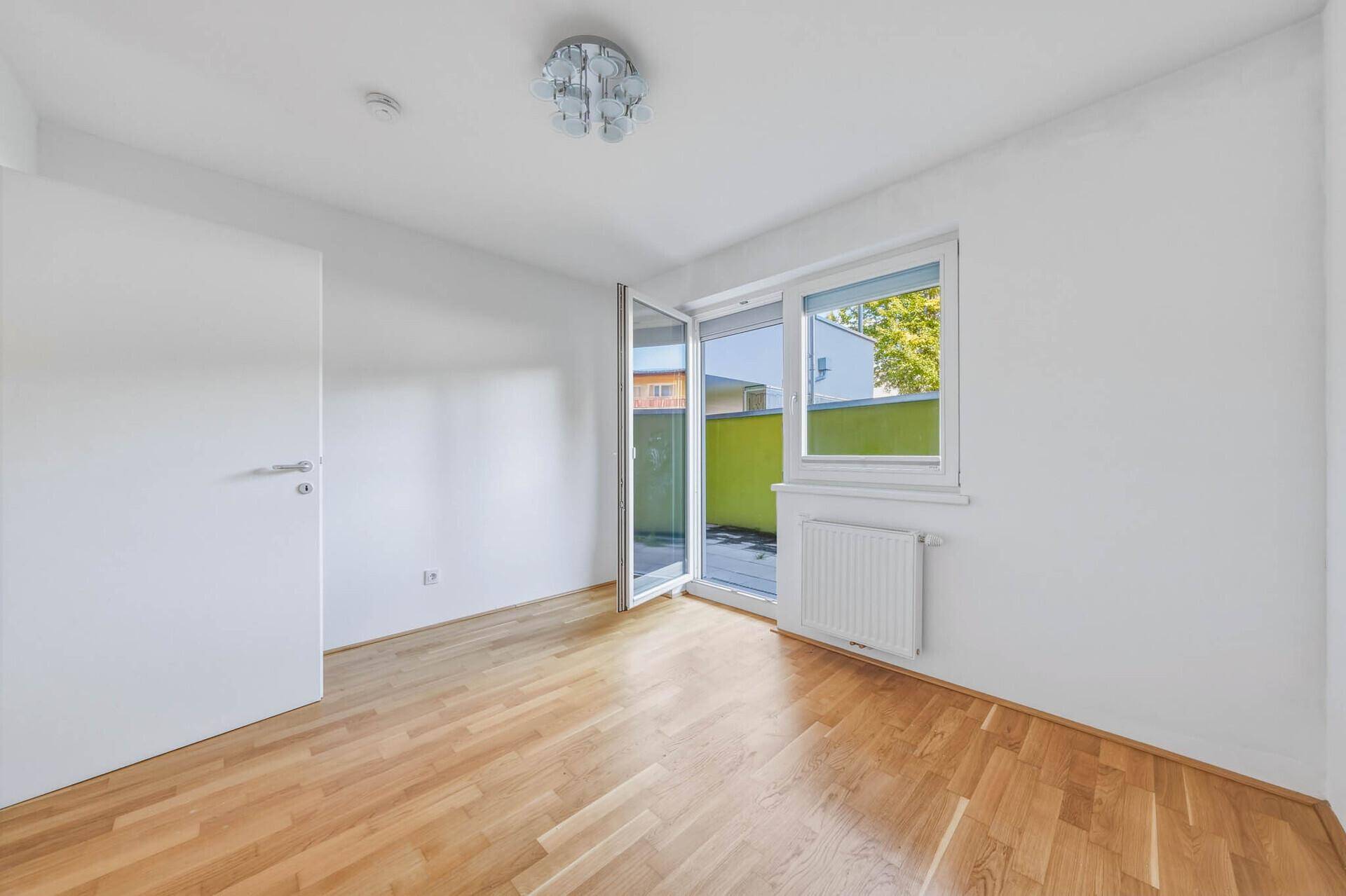 Schlafzimmer mit Parkettboden und Zugang zu einem kleinen Balkon oder einer Terrasse.