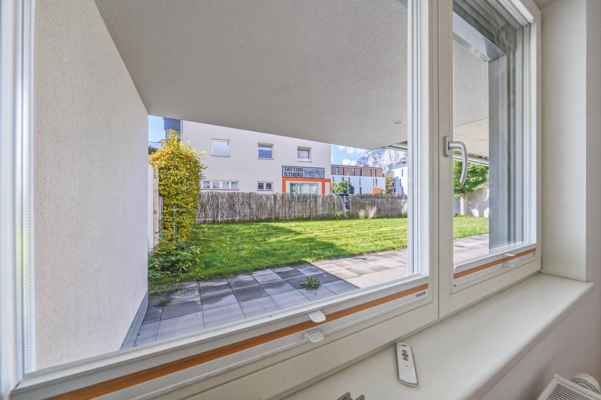 Blick aus dem Fenster auf den privaten Gartenbereich mit Terrasse und grüner Hecke.