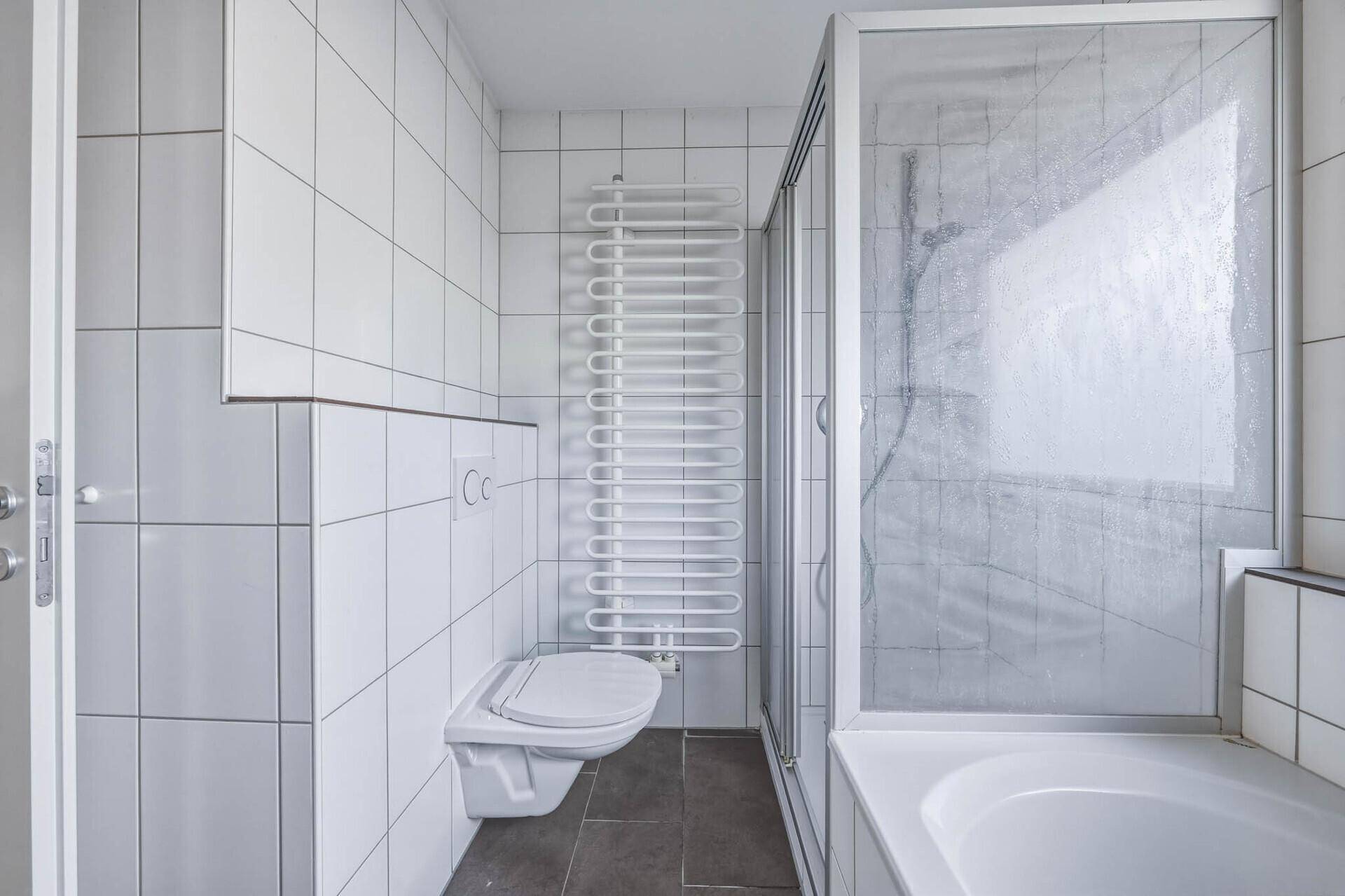 Badezimmer mit Duschkabine, wandhängendem WC und beheiztem Handtuchhalter.