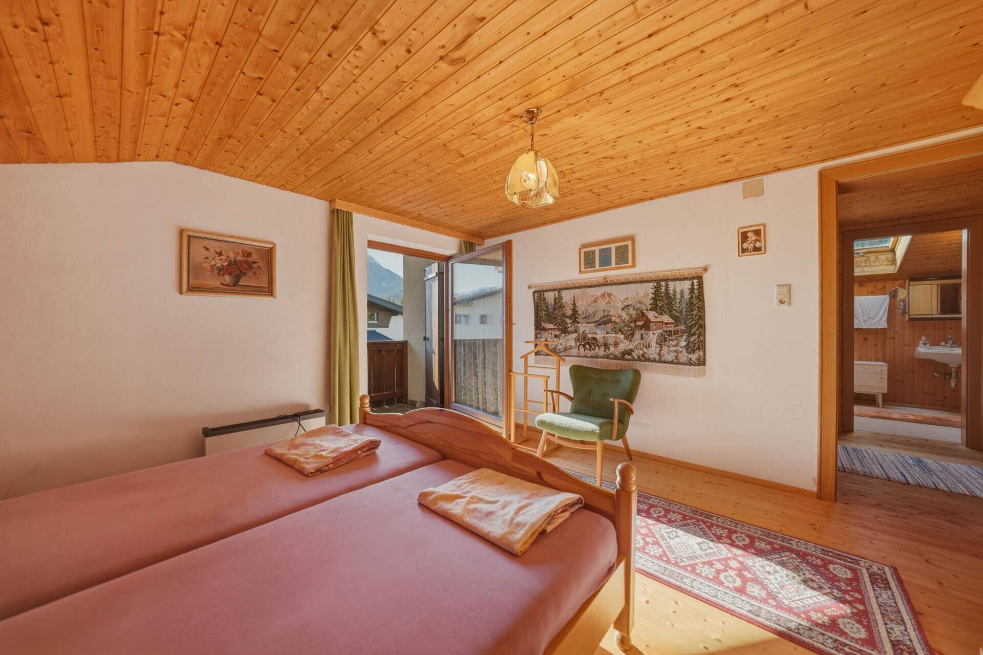 Schlafzimmer mit Holzdecke und -wänden, Doppelbett und Zugang zu einem Balkon.