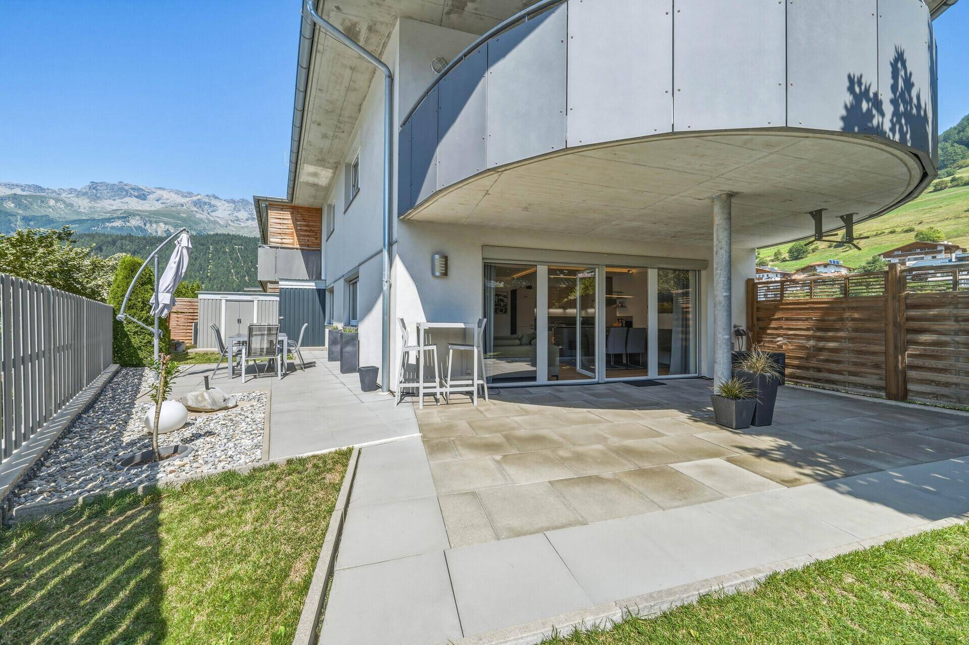 Ansicht des Gebäudes mit großer Terrasse, Garten und Balkon, umgeben von Bergen.