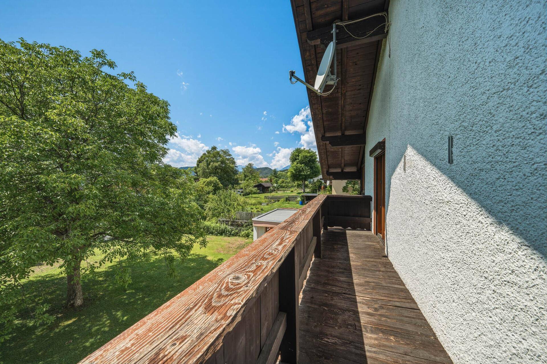 Geräumiger Holzbalkon mit weitem Blick über die grüne Landschaft und die Berge.