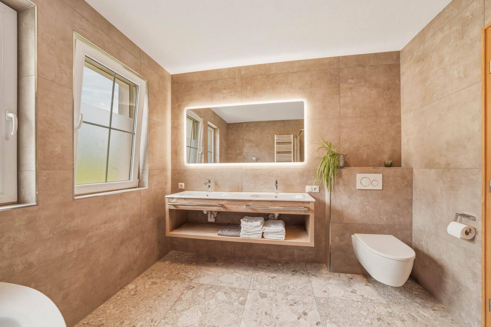 Modernes Badezimmer mit Doppelwaschbecken, beleuchtetem Spiegel und wandhängendem WC.