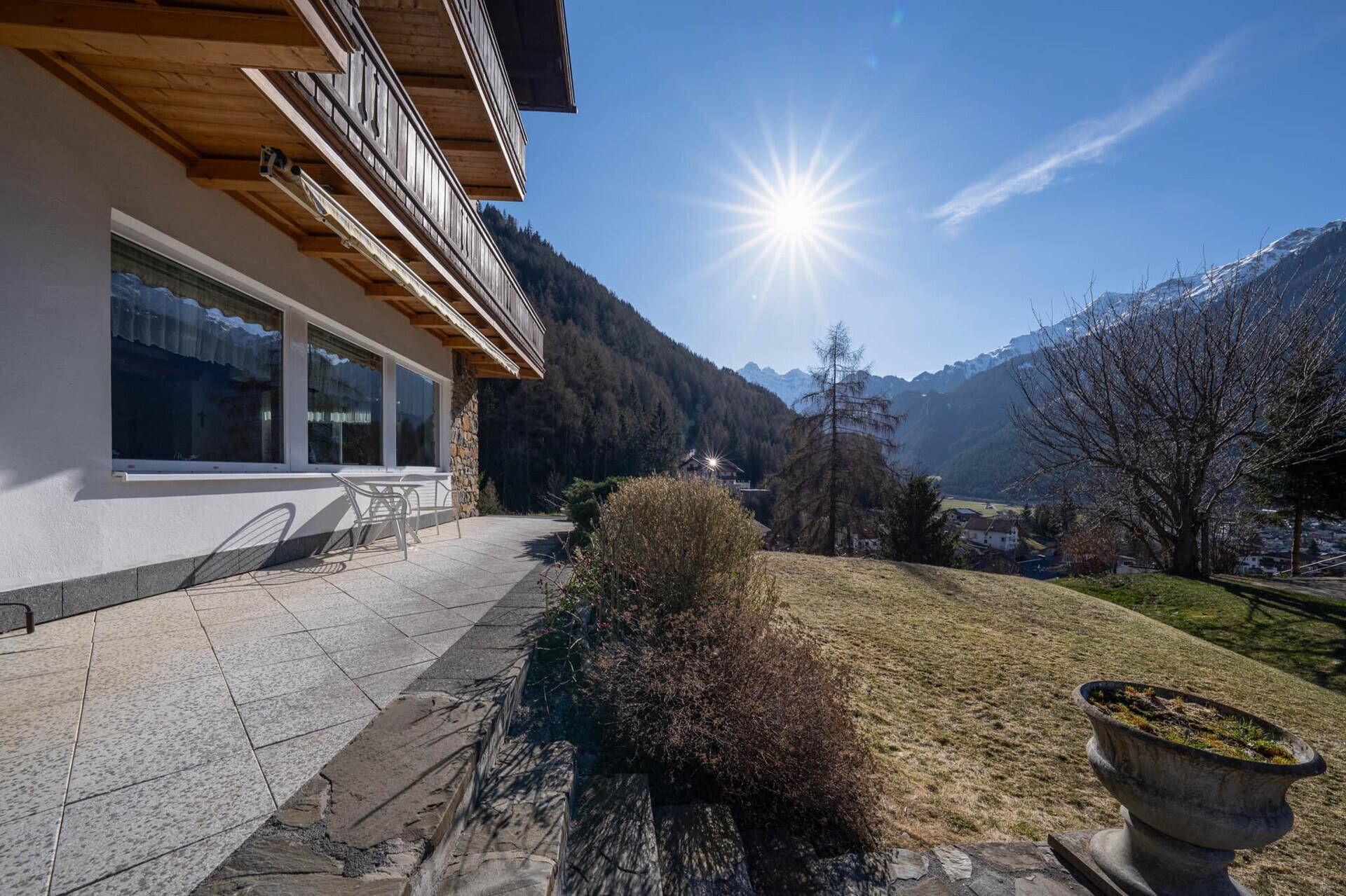 Sonniger Terrassenbereich mit Fliesenboden und Blick auf die Berge.