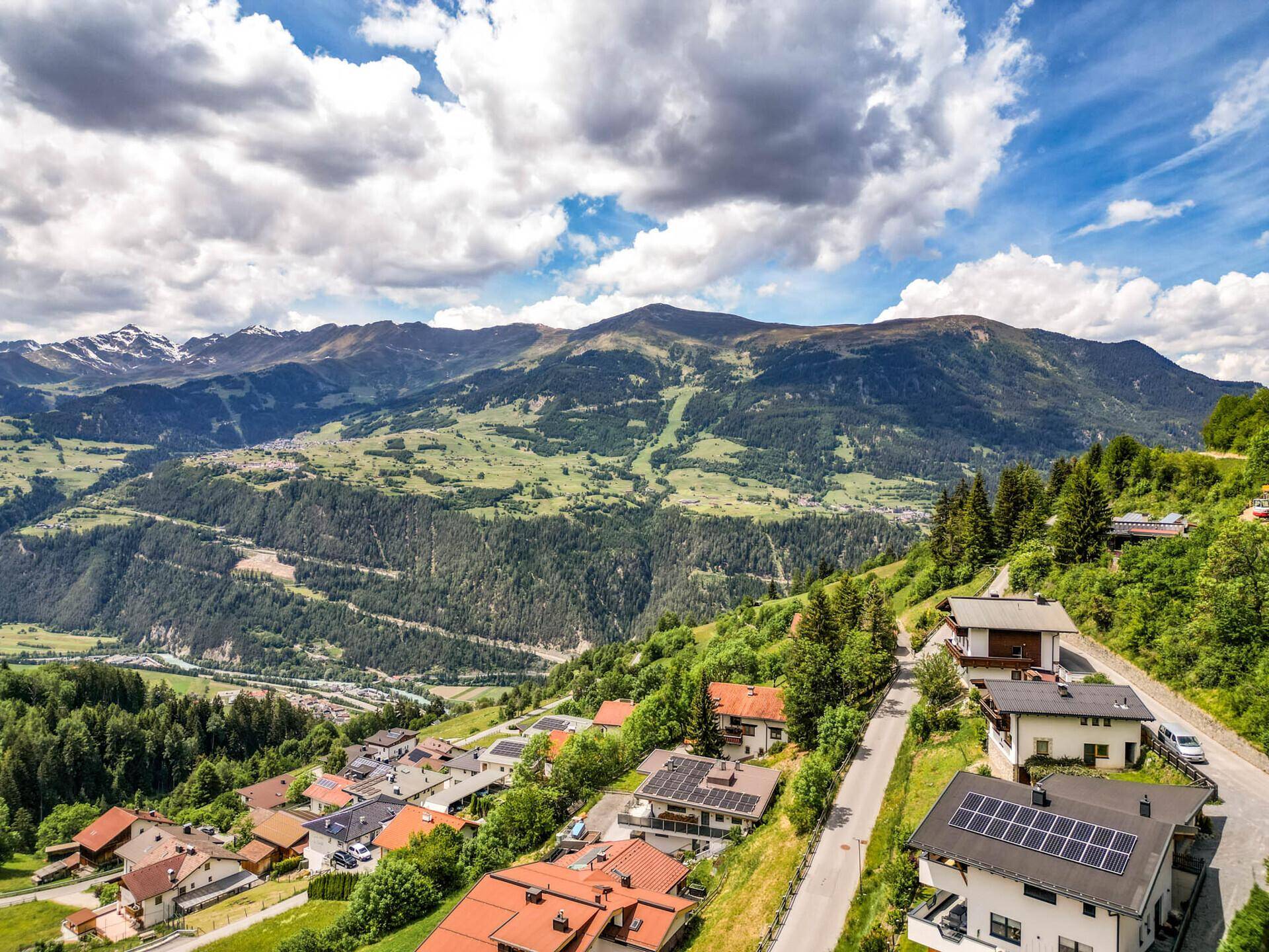 Häuser am Berghang mit Solaranlagen auf den Dächern und weitem Blick auf die Alpen.