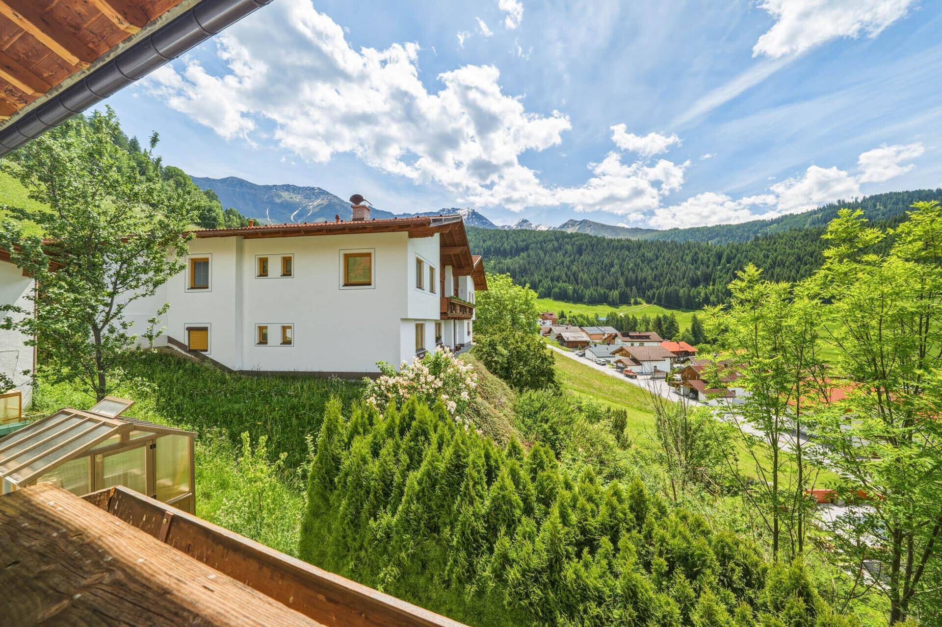 Weitläufiger Blick von der Terrasse auf ein Haus am Hang und die umliegende Berglandschaft.