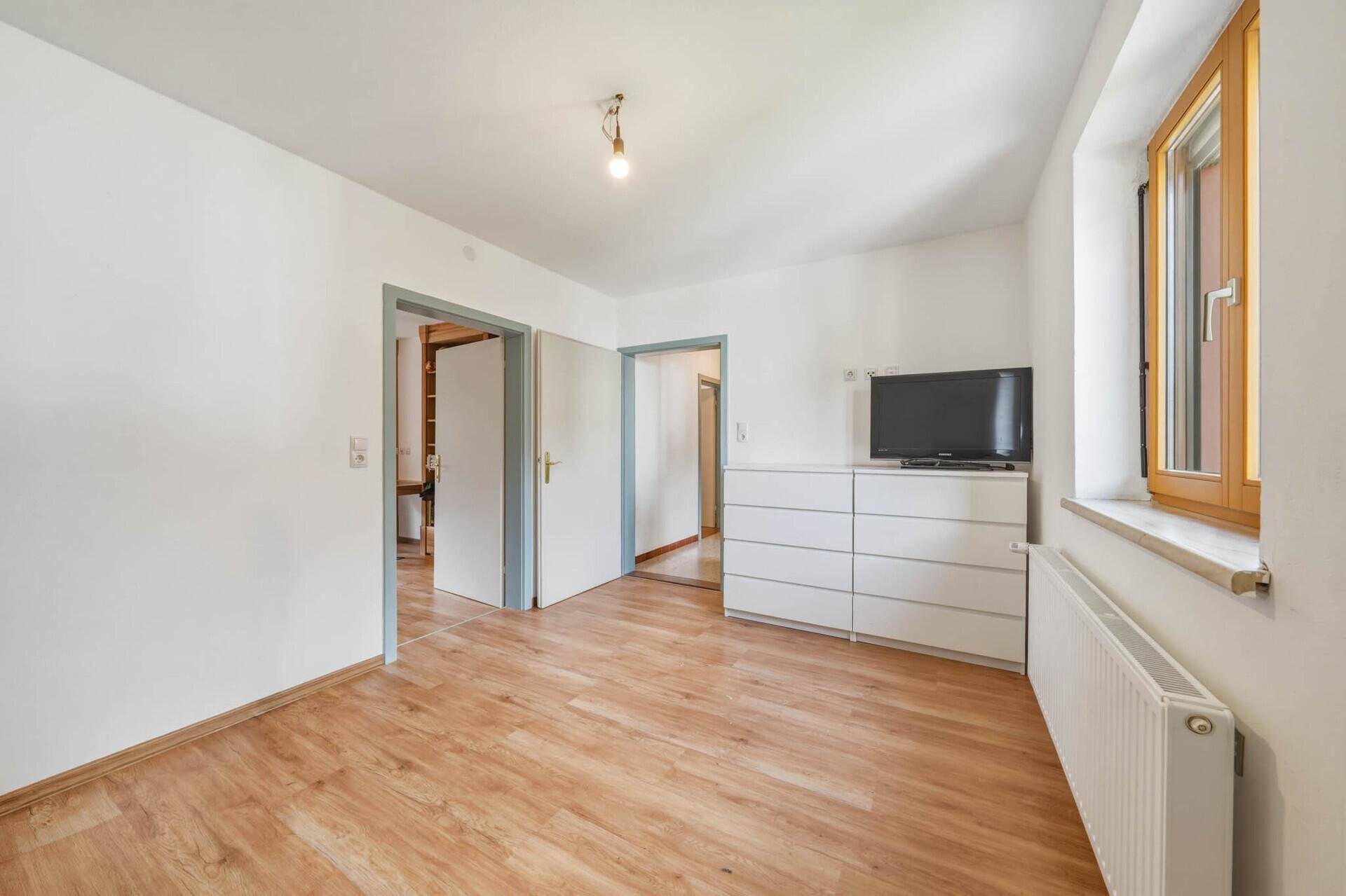 Helles, leeres Zimmer mit Laminatboden, weiß gestrichenen Wänden und einem Fenster.