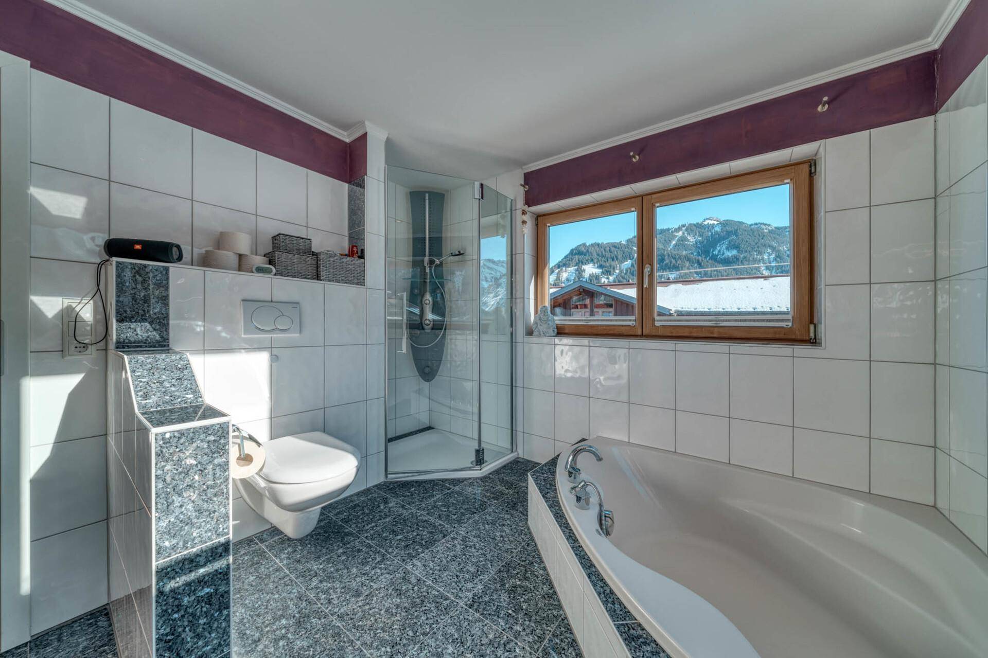 Helles Badezimmer mit Badewanne, Dusche und Fenster mit Bergblick.