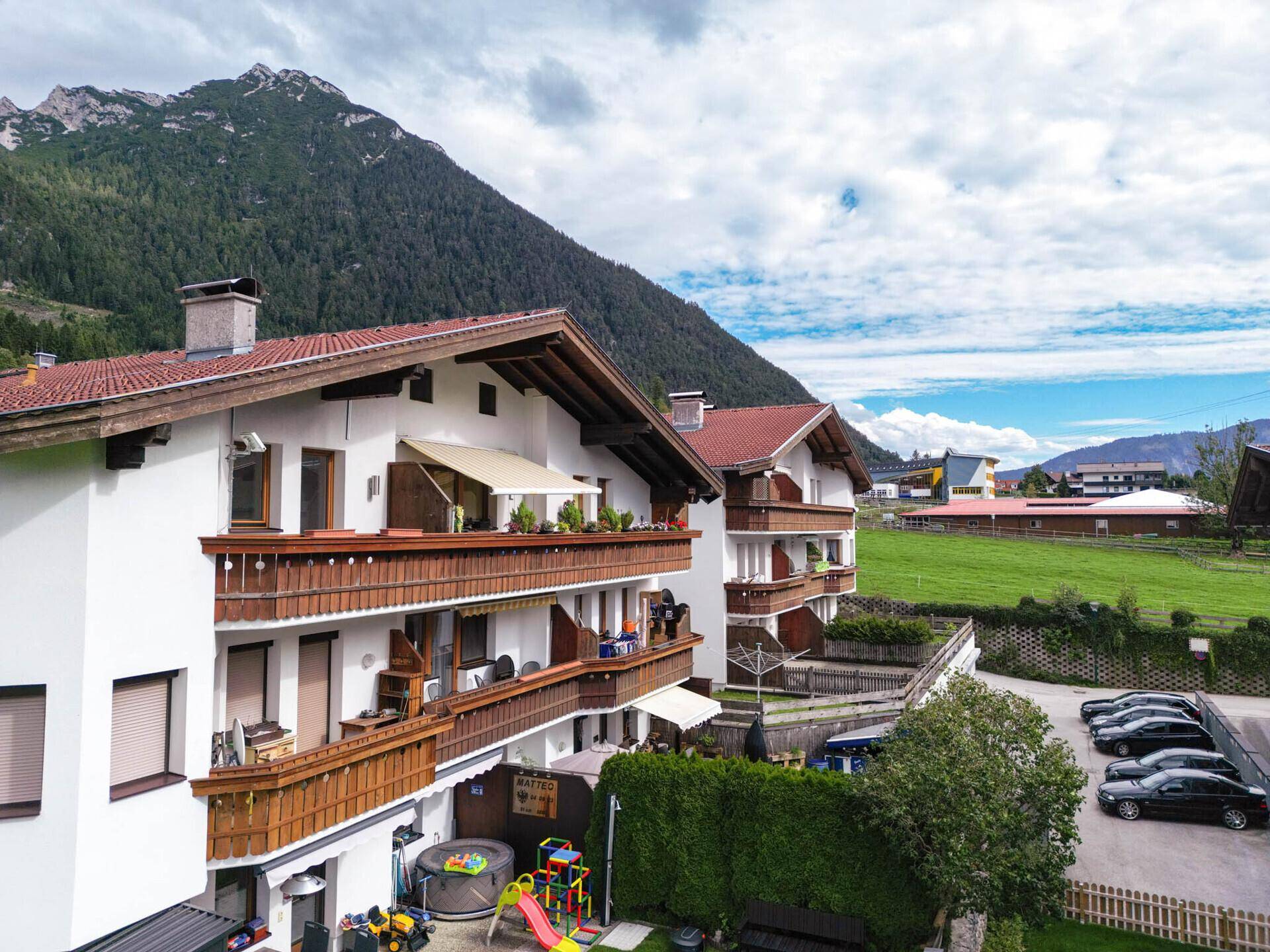 Mehrfamilienhaus in den Alpen mit Parkplätzen und weitem Blick auf die umliegende Landschaft.