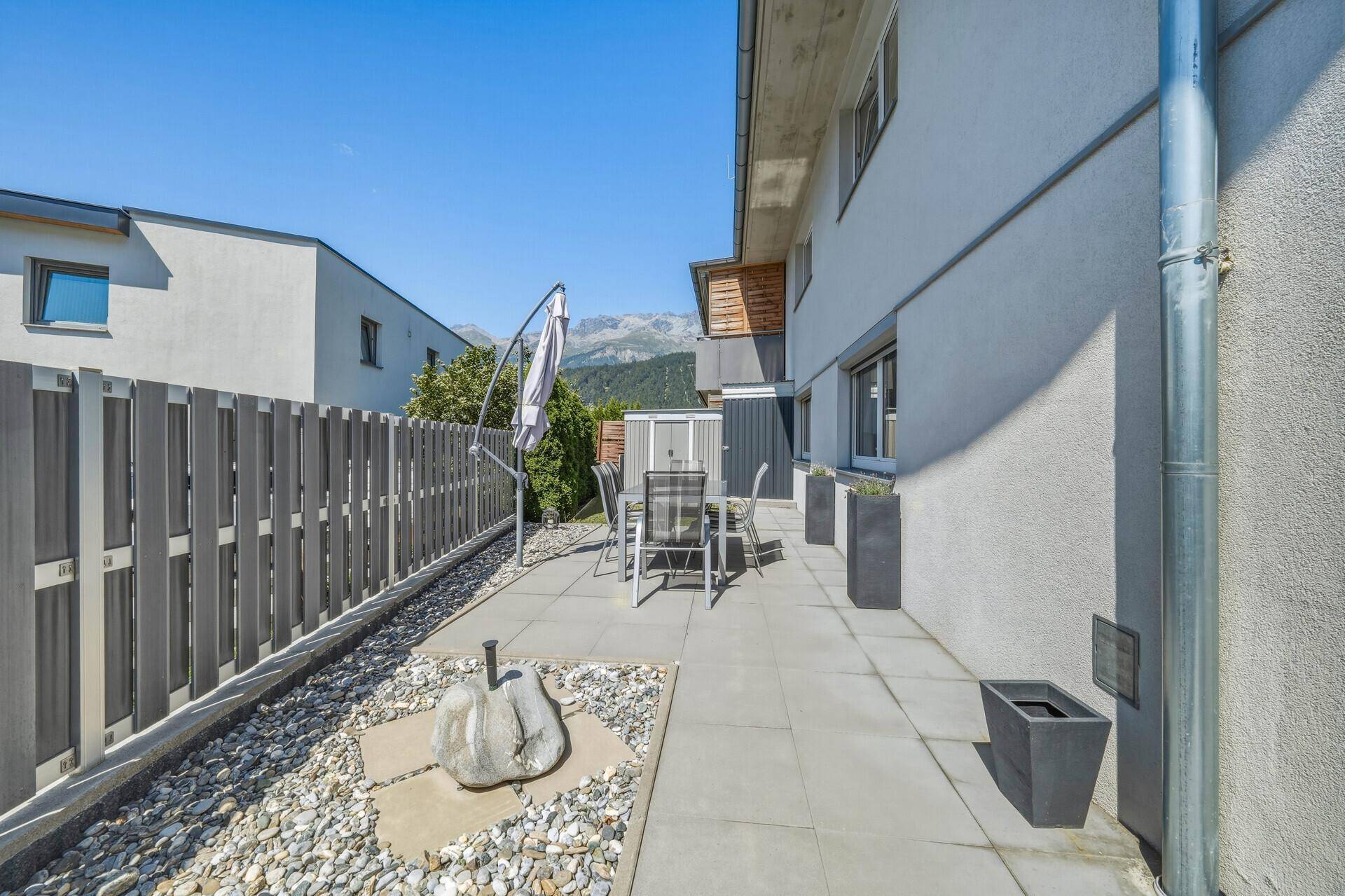 Sonnige Terrasse mit Gartenmöbeln, Kiesbeet und Blick auf die umliegende Berglandschaft.