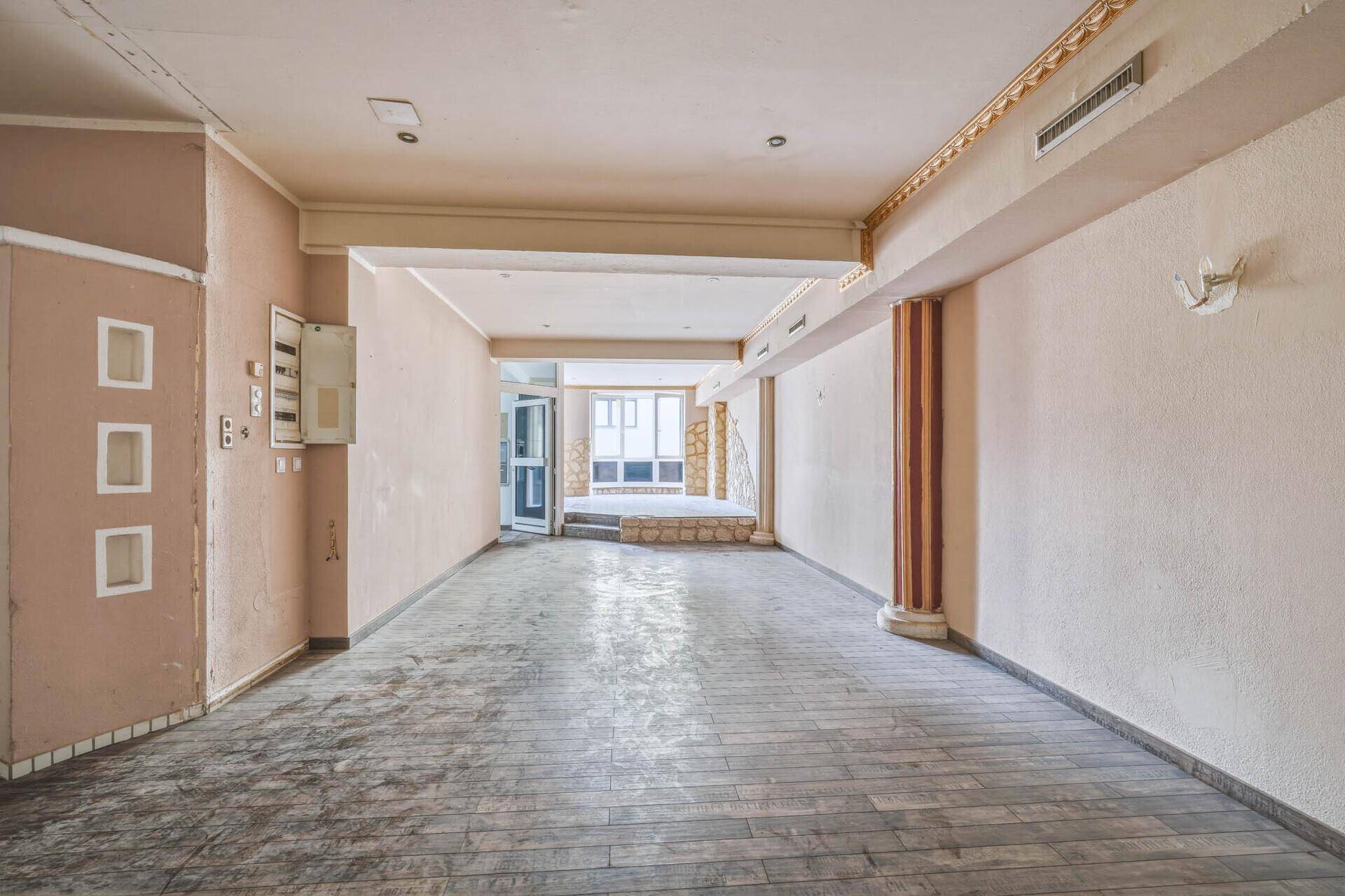 Langer, leerstehender Gewerberaum mit Holzboden, Schalttafel und Blick auf den Eingangsbereich.