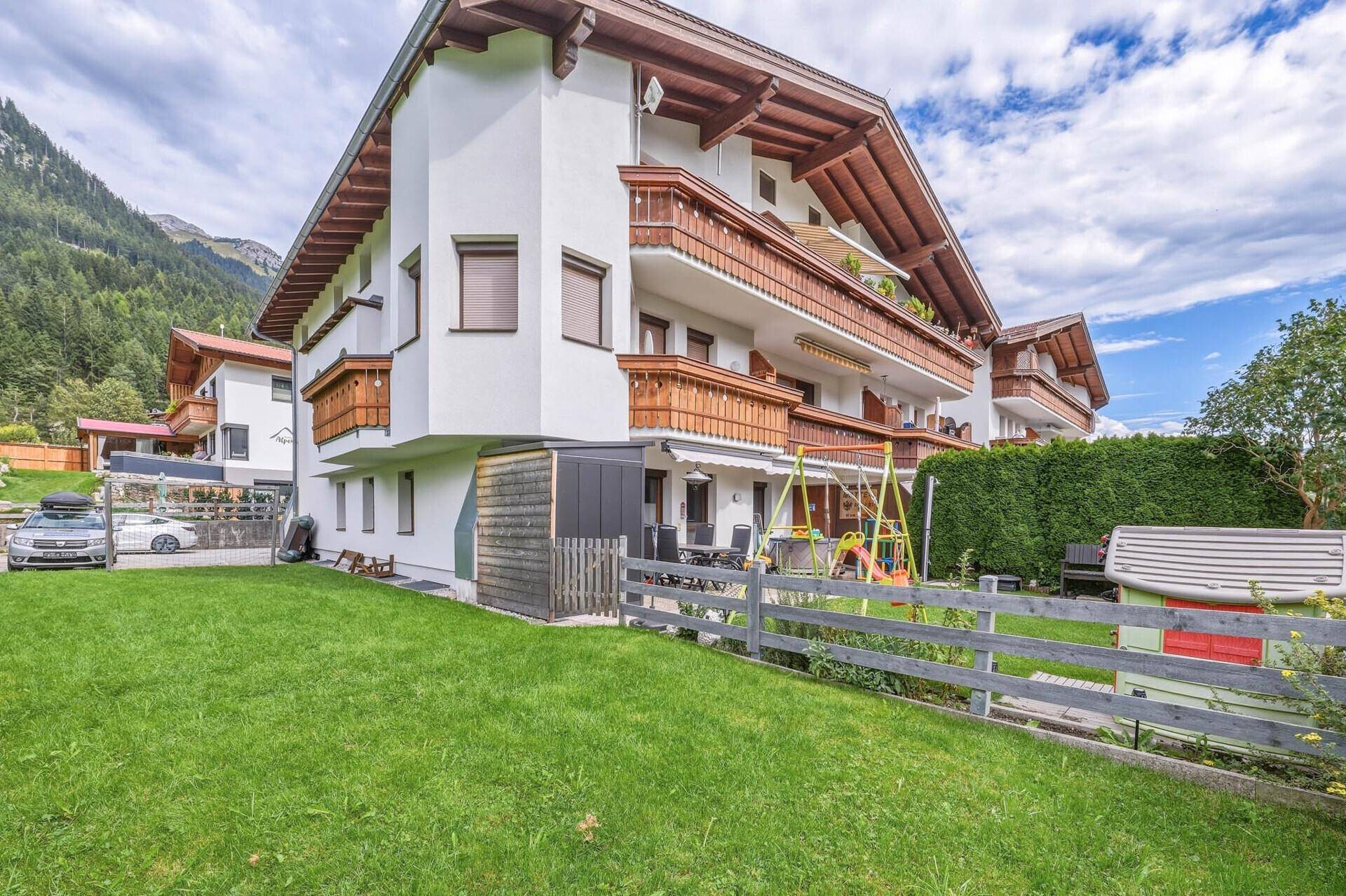 Gepflegter Gartenbereich mit Rasenfläche, Holzzaun und Spielgeräten neben dem Wohnhaus.