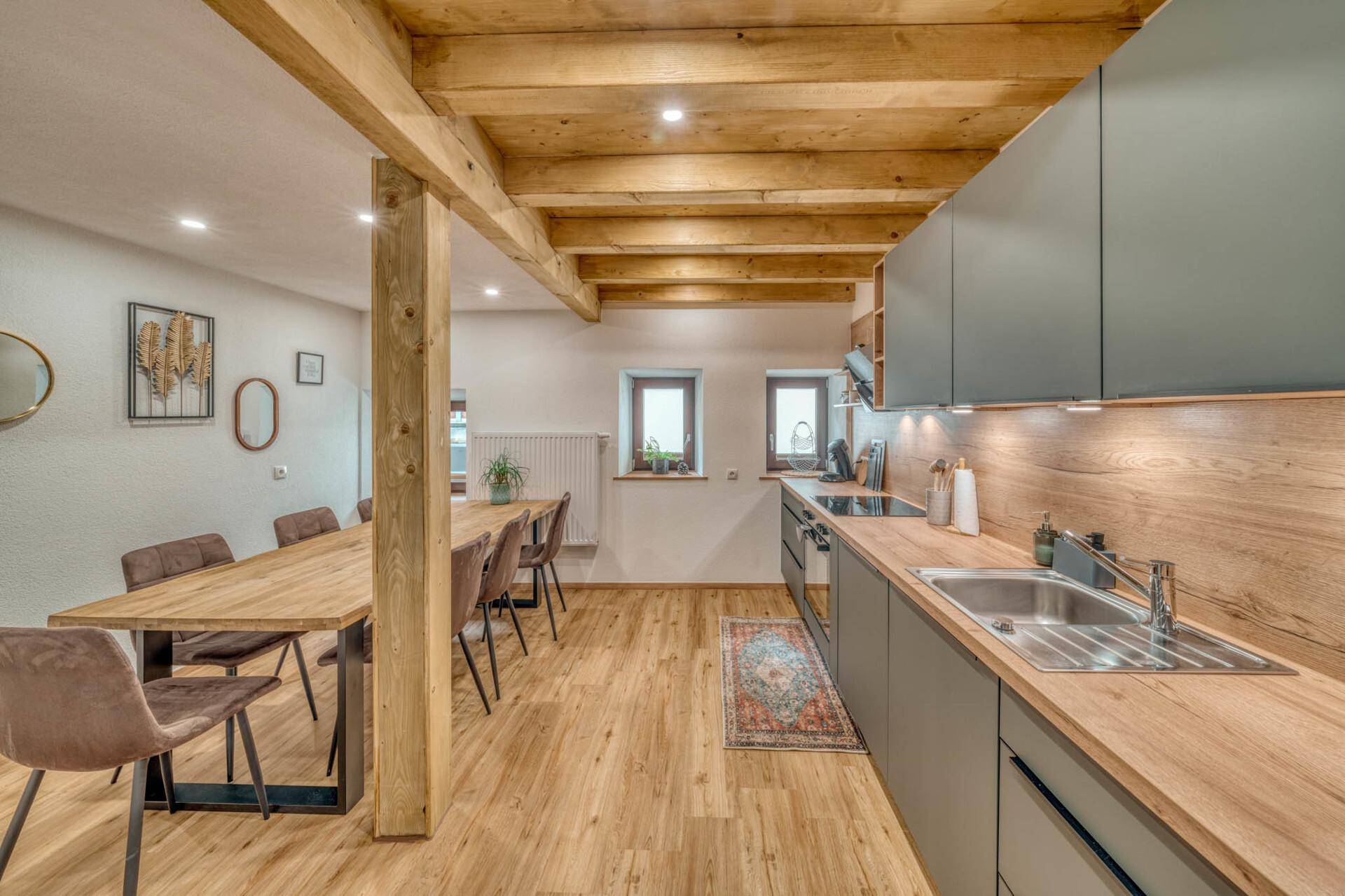 Moderne offene Küche mit Essbereich, Holzbalken und Holzboden, hell und geräumig.