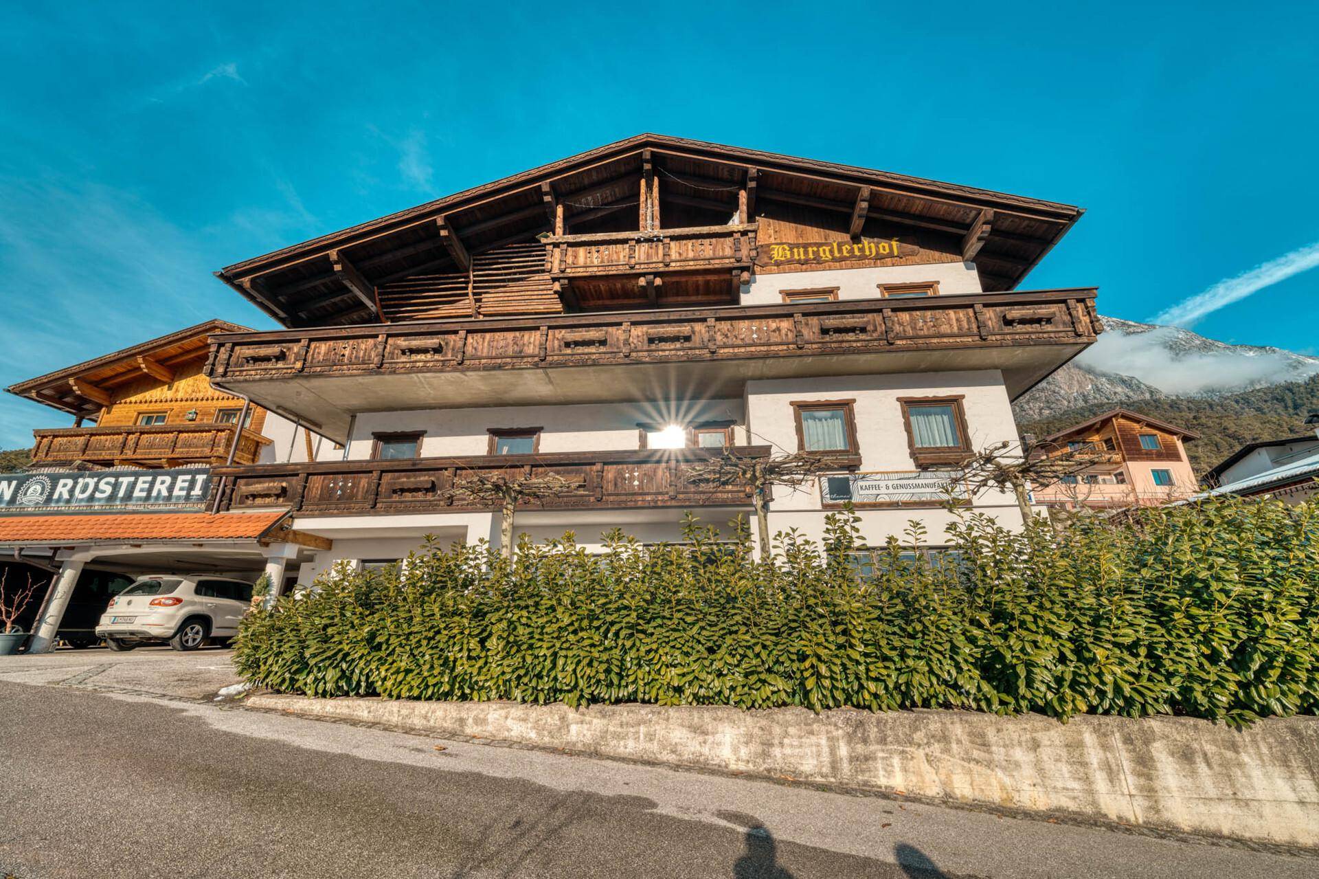 Traditionelles Gebäude im alpinen Stil mit Holzbalkonen und gepflegter Hecke.