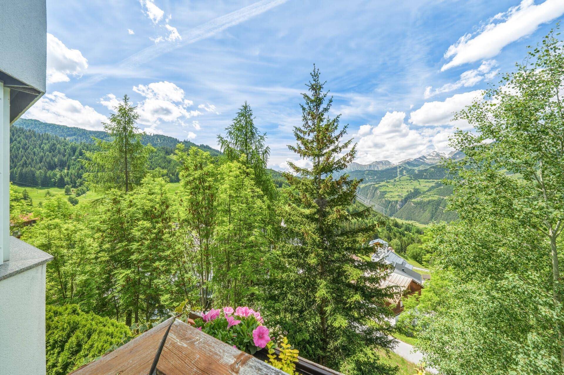 Panoramablick von einem Balkon auf ein grünes Tal mit Wäldern und fernen Bergen.
