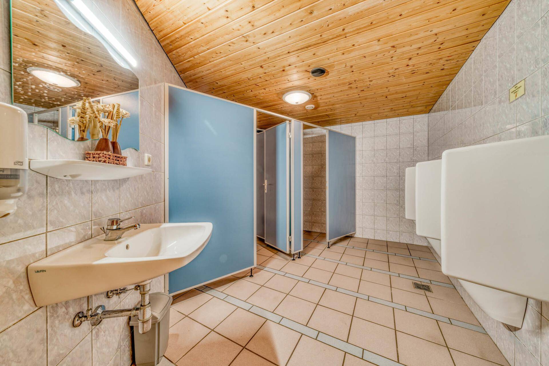 Toilettenbereich mit Waschbecken, Urinalen und blauen Trennwänden.