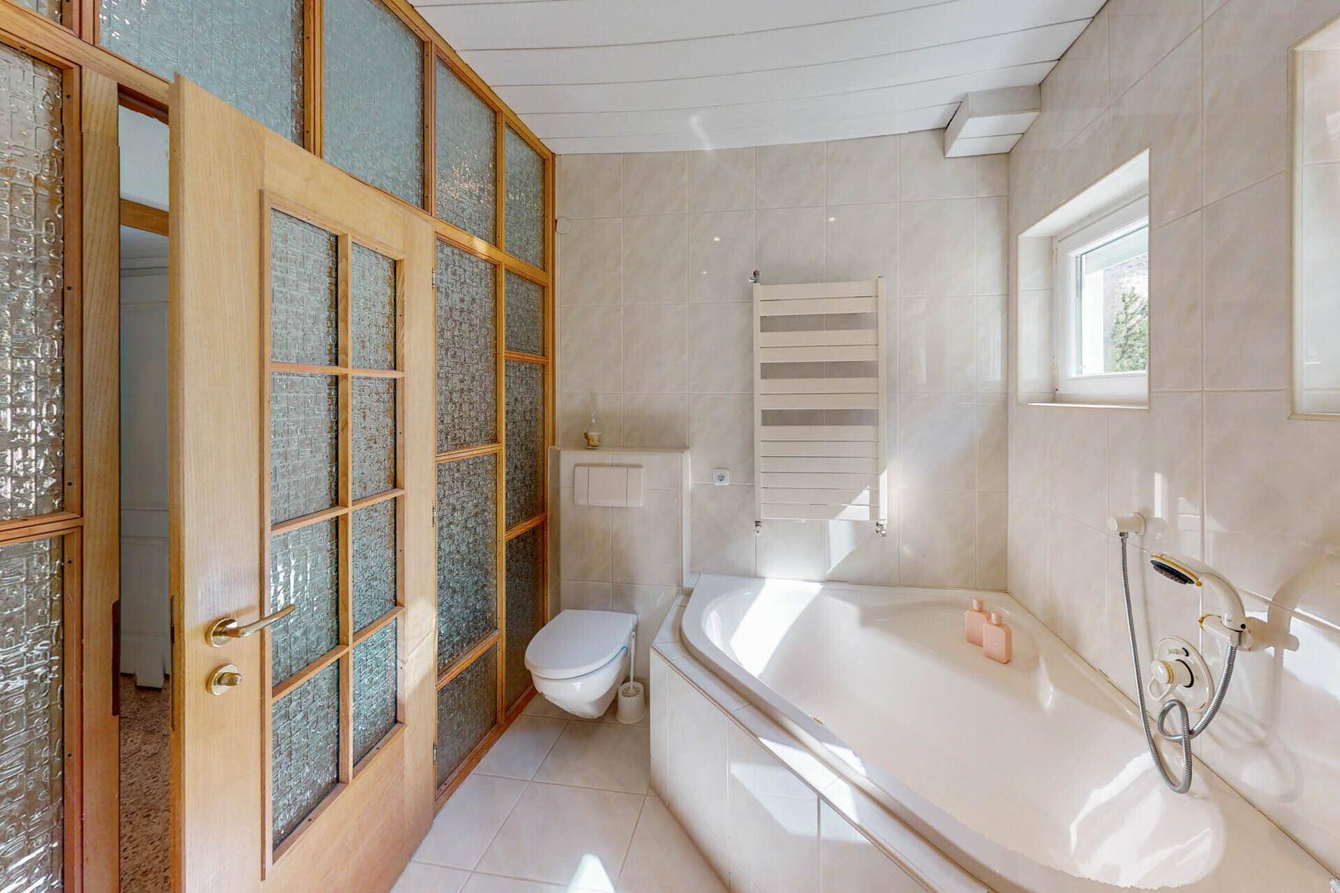 Helles Badezimmer mit Badewanne, WC und Fliesen in neutralen Farben.