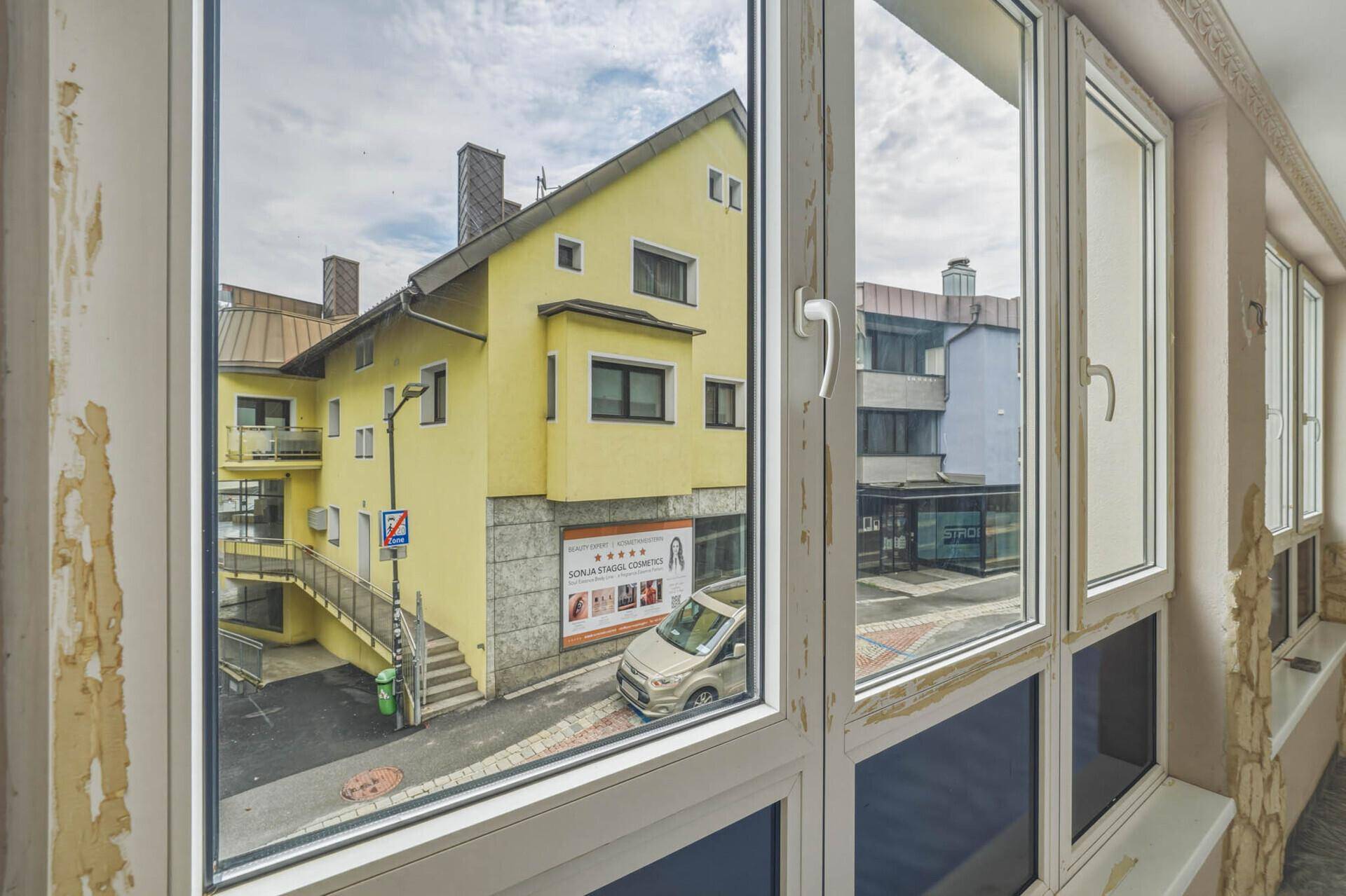 Fensterfront mit Blick auf ein gelbes Gebäude und die umliegende städtische Bebauung.