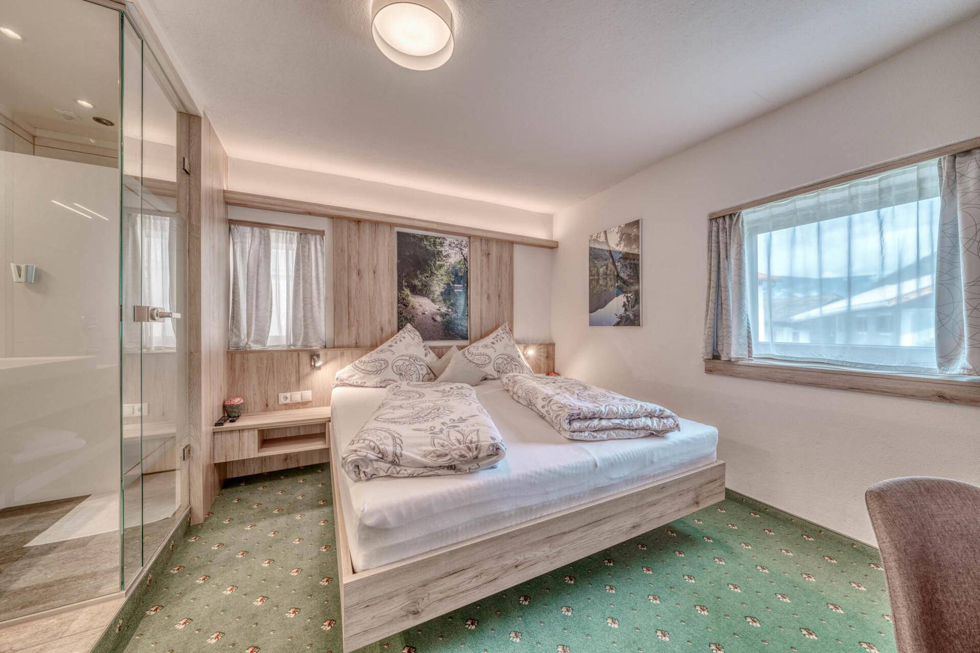 Modernes Schlafzimmer mit Doppelbett und offenem Badezimmerbereich, helle Einrichtung und Teppichboden.