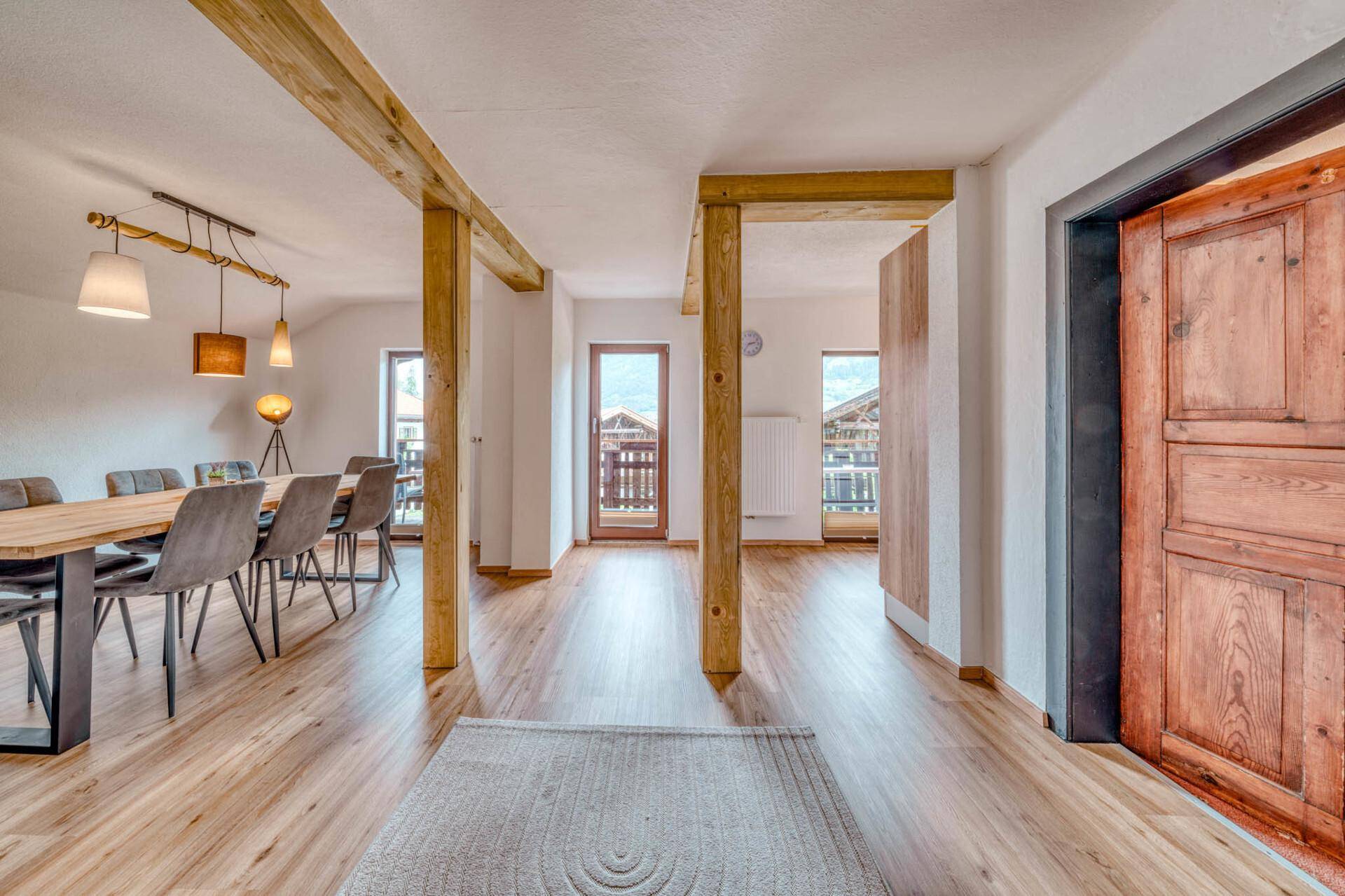 Heller Essbereich mit Holzbalken, großem Esstisch und Zugang zu einem Balkon.