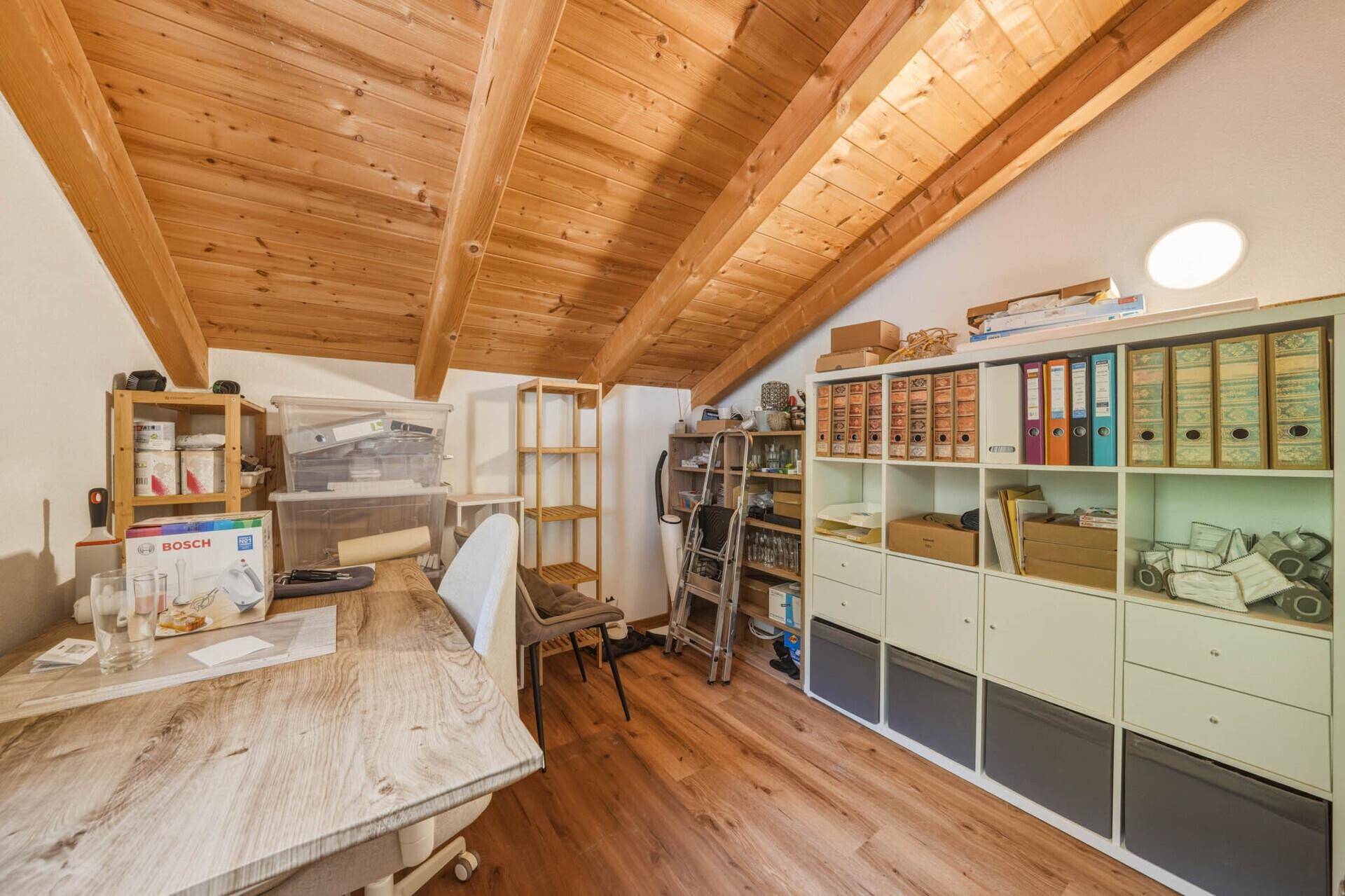 Arbeitszimmer im Dachgeschoss mit Holzbalkendecke, Holzboden und Regalen für Stauraum.