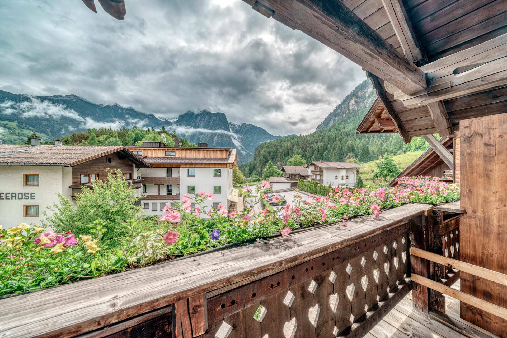 Breiter Holzbalkon mit Blumenkästen und einem weiten Blick auf die Alpen und das Tal.