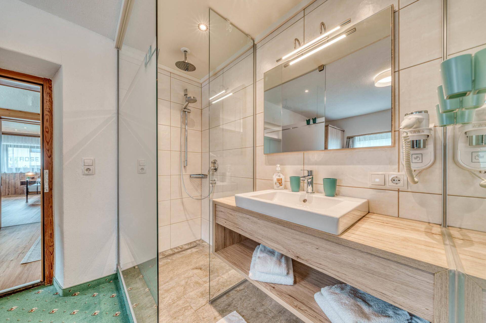 Helles Badezimmer mit begehbarer Dusche, modernem Waschbecken und Holzwaschtisch.