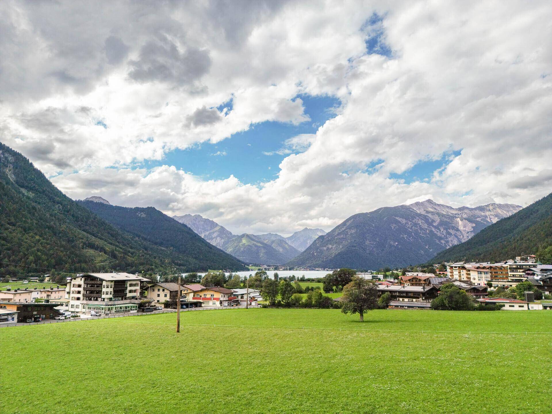 Weitläufiger Panoramablick auf eine alpine Seenlandschaft mit umliegenden Dörfern und Bergen.