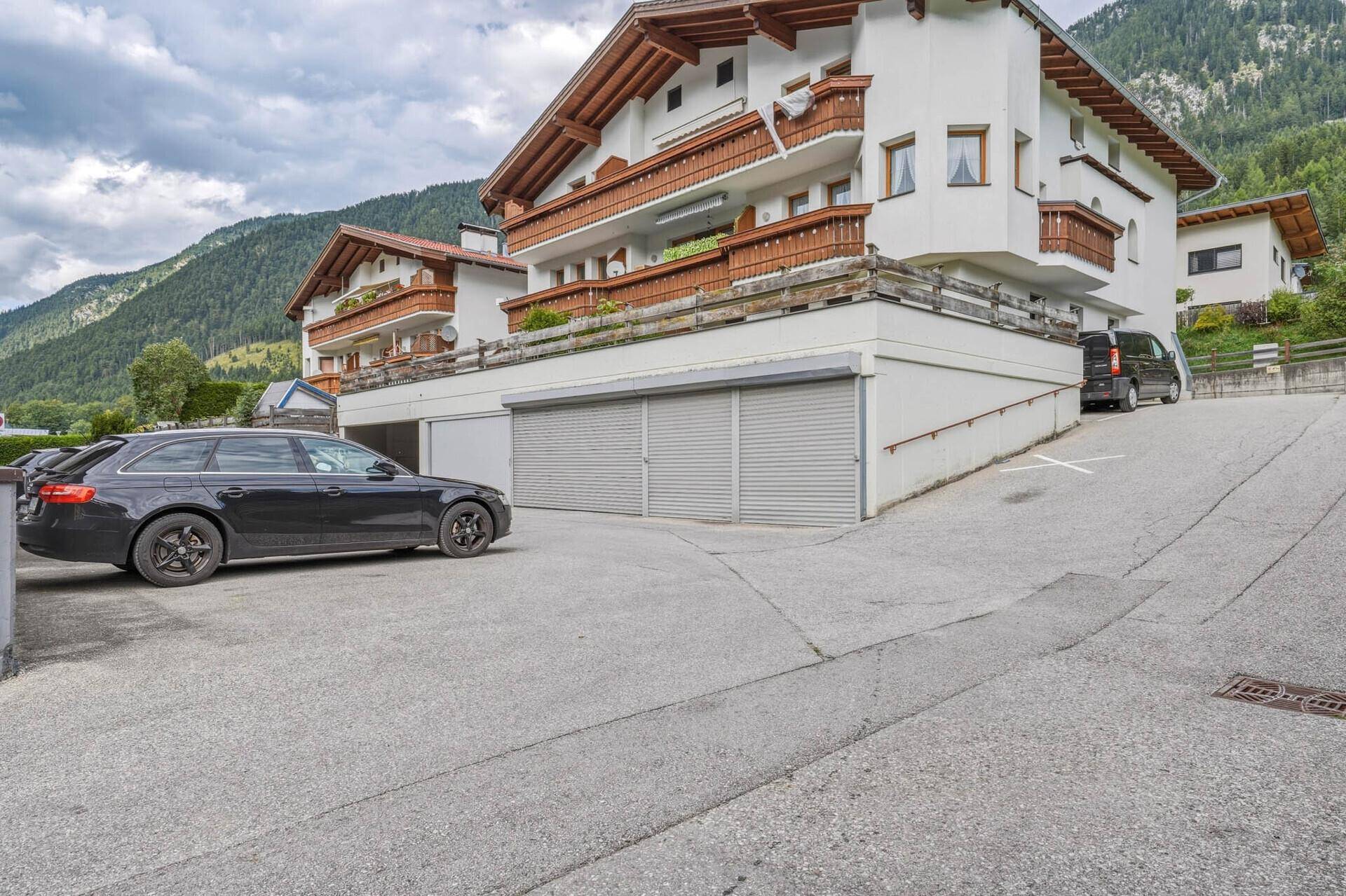 Vorderansicht des Gebäudes mit Zufahrt zur Tiefgarage und einem geparkten Fahrzeug.