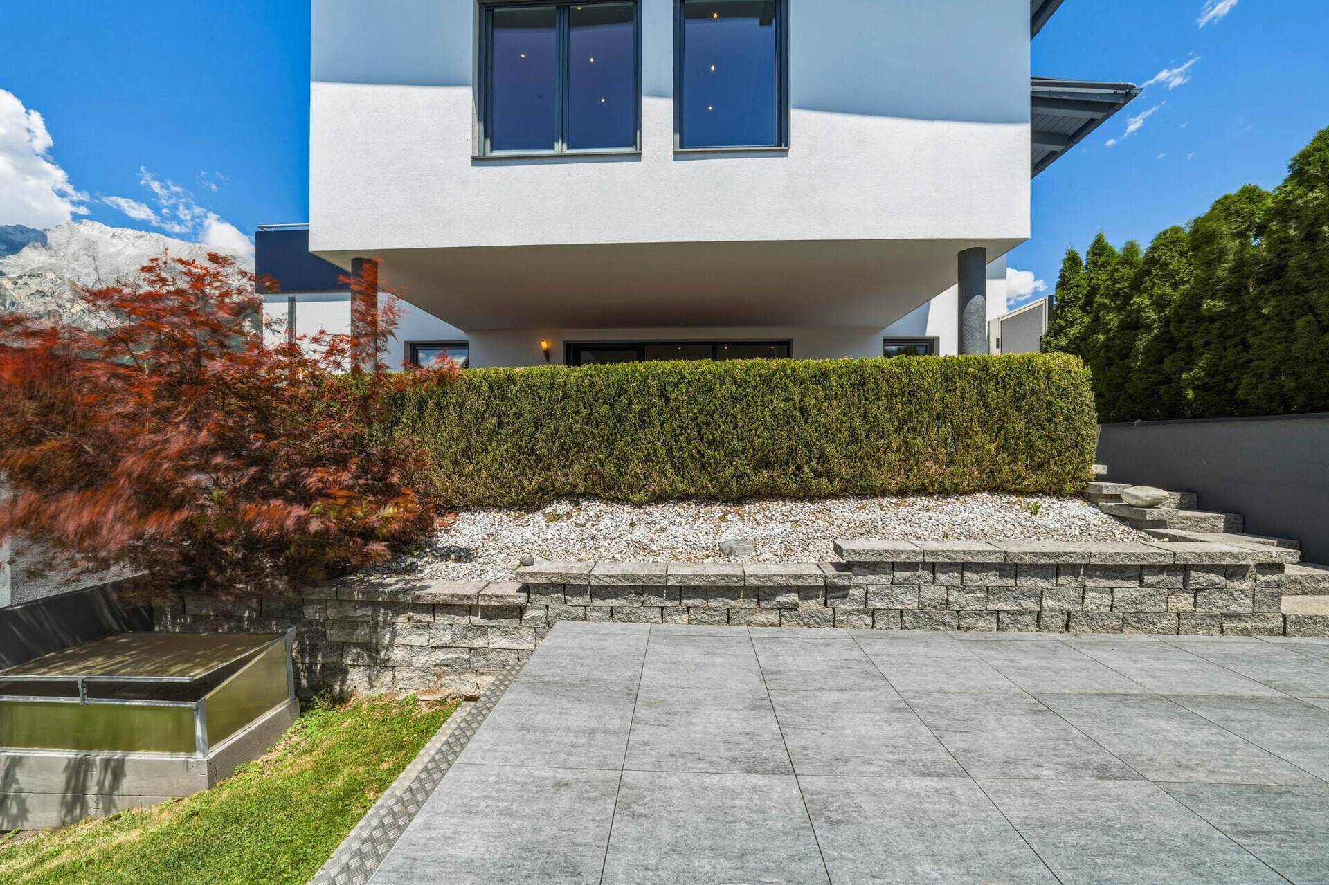 Moderne Hausfassade mit gepflastertem Außenbereich, Stützmauern und Treppen.