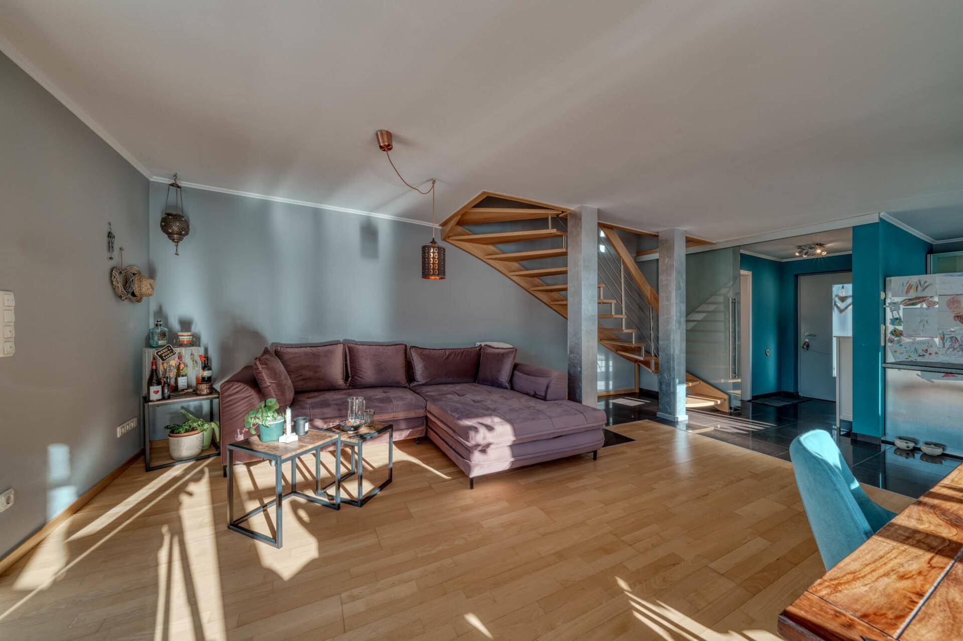 Heller Wohnbereich mit bequemer Eckcouch, Holzboden und offener Treppe.