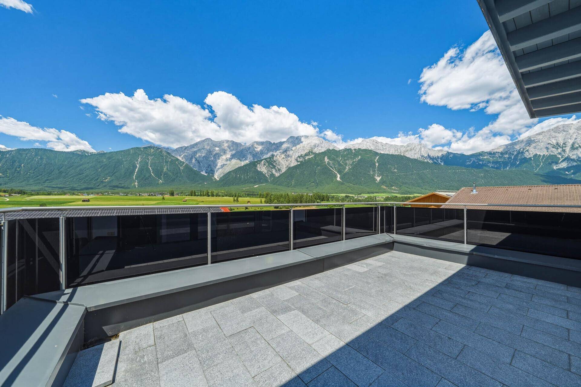 Sonnige Dachterrasse mit modernem Glasgeländer und beeindruckendem Bergblick.