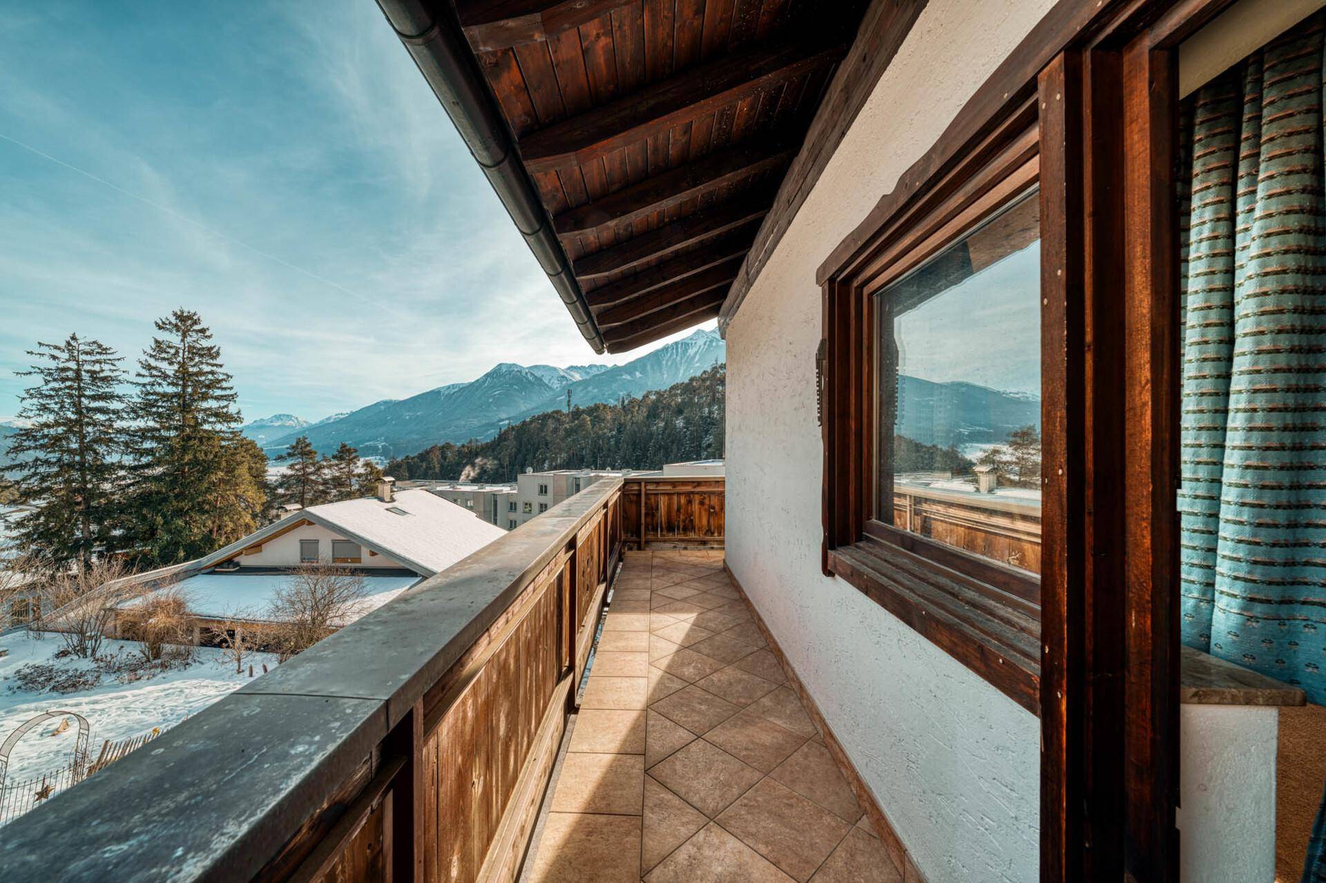 Langer Balkon mit Fliesenboden und Holzbalkonbrüstung mit Bergblick.