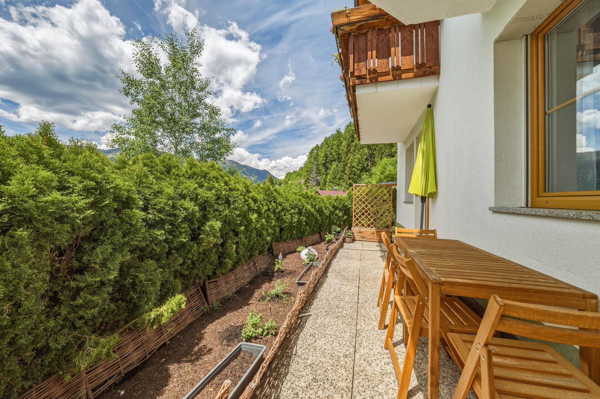 Gemütliche Terrasse mit Holzmöbeln und Sonnenschirm, umgeben von einer hohen Hecke für Privatsphäre.