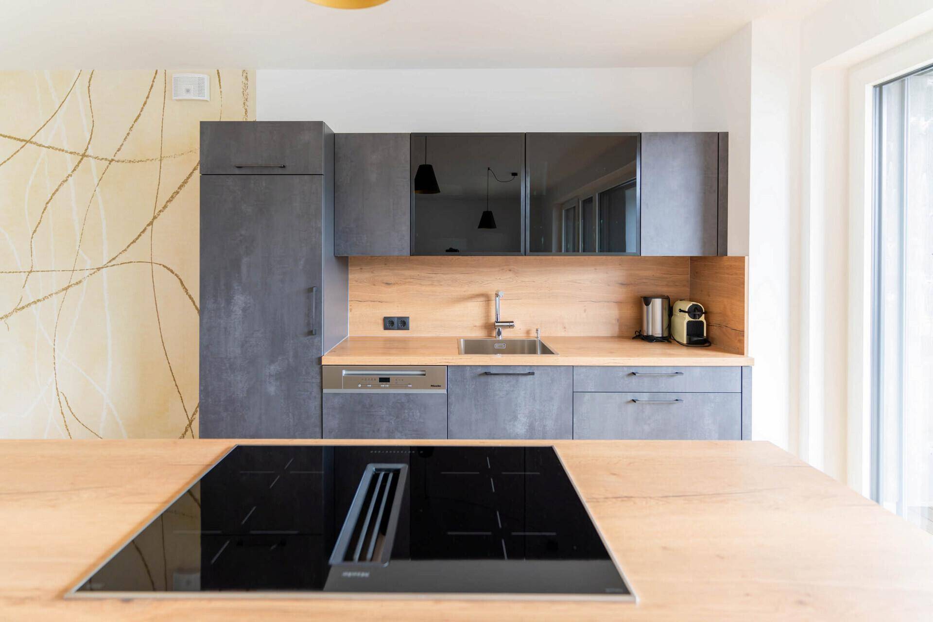 Moderne Küche mit grauen Fronten, Holzarbeitsplatte und integriertem Induktionskochfeld.
