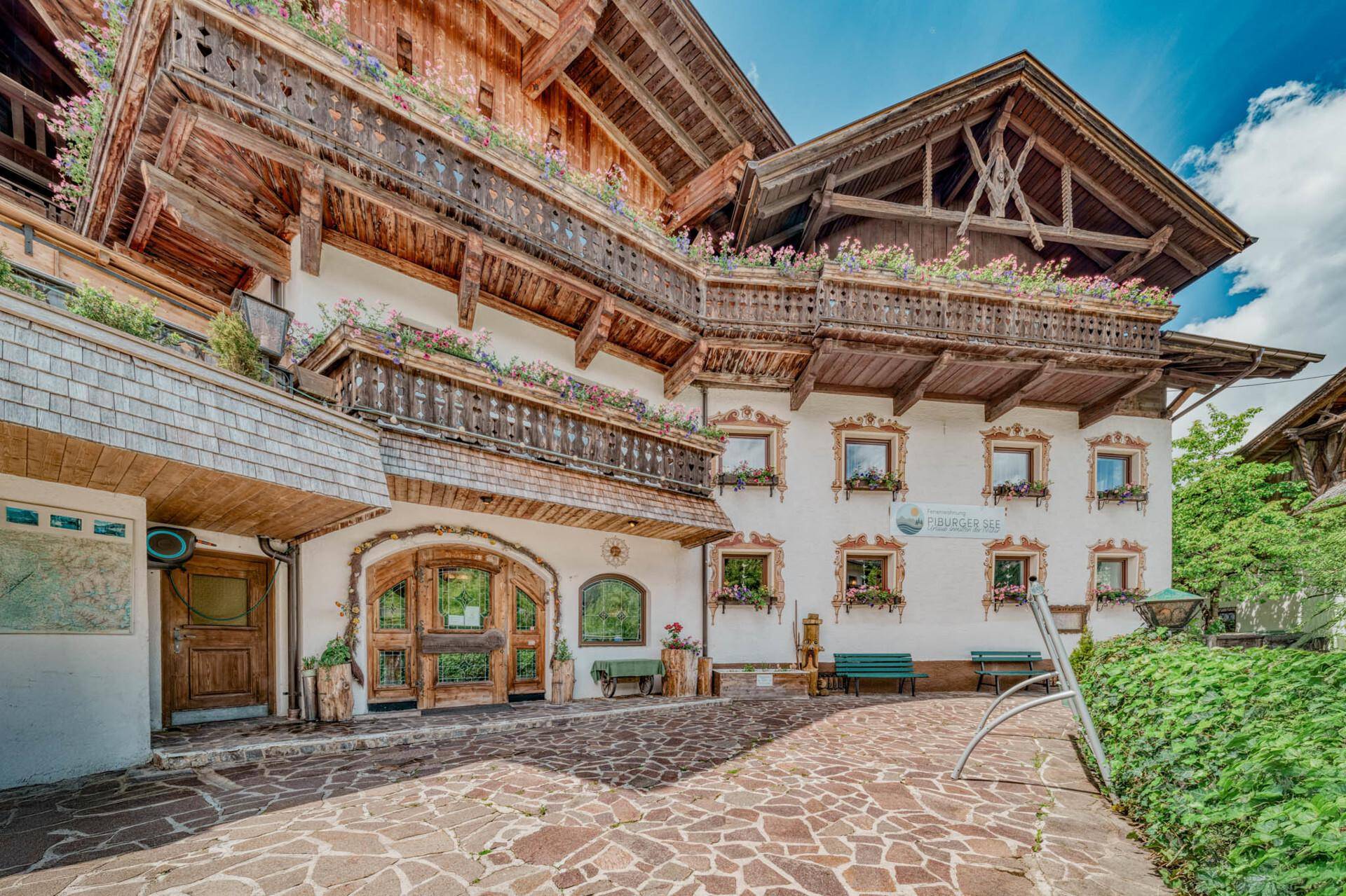 Traditionelles Gebäude mit mehreren Balkonen, Blumenkästen und gepflastertem Vorplatz.