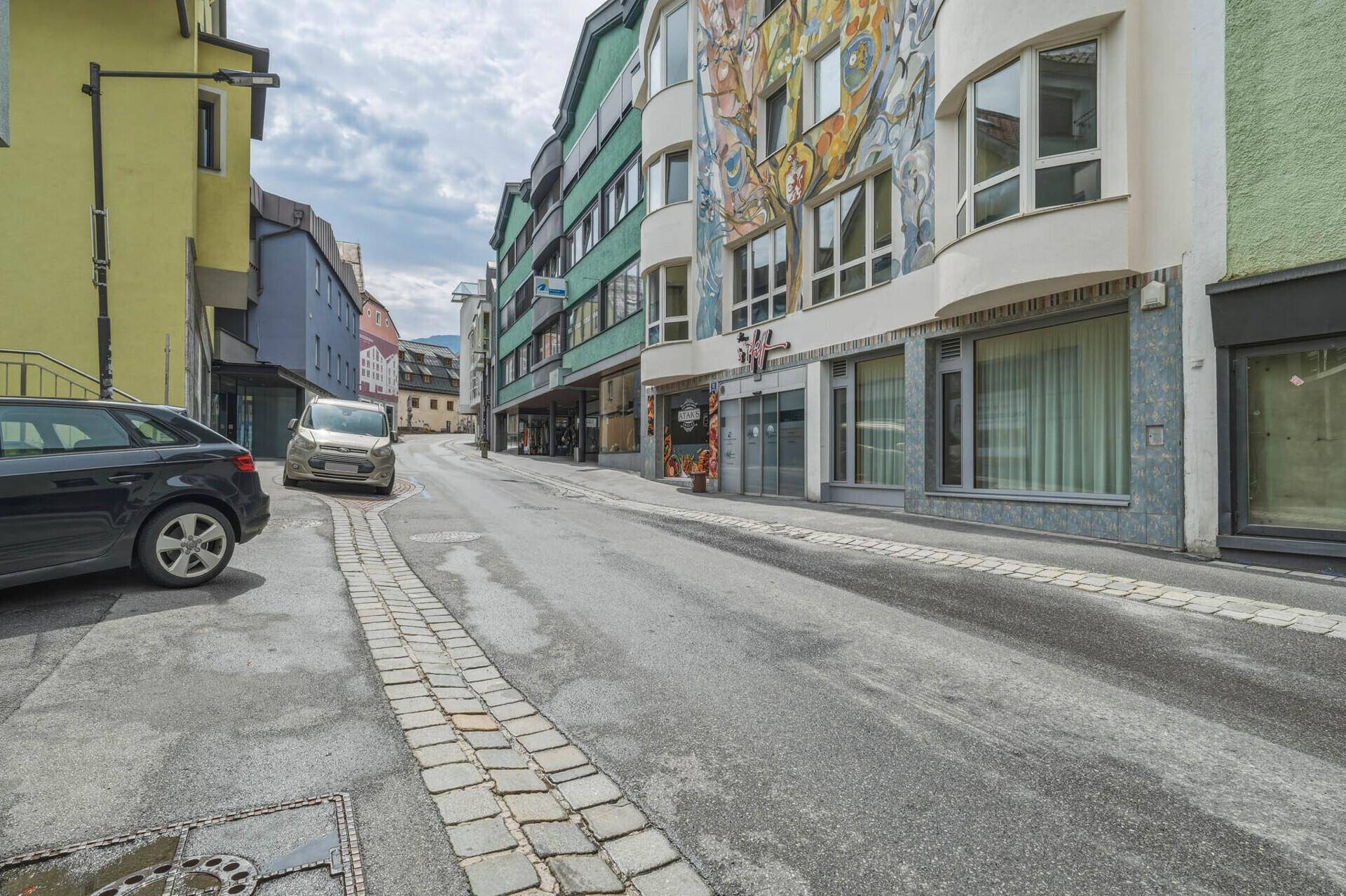 Eine weitere Perspektive der Straße mit geparkten Autos und dem Gebäude mit der farbenfrohen Fassadenmalerei.