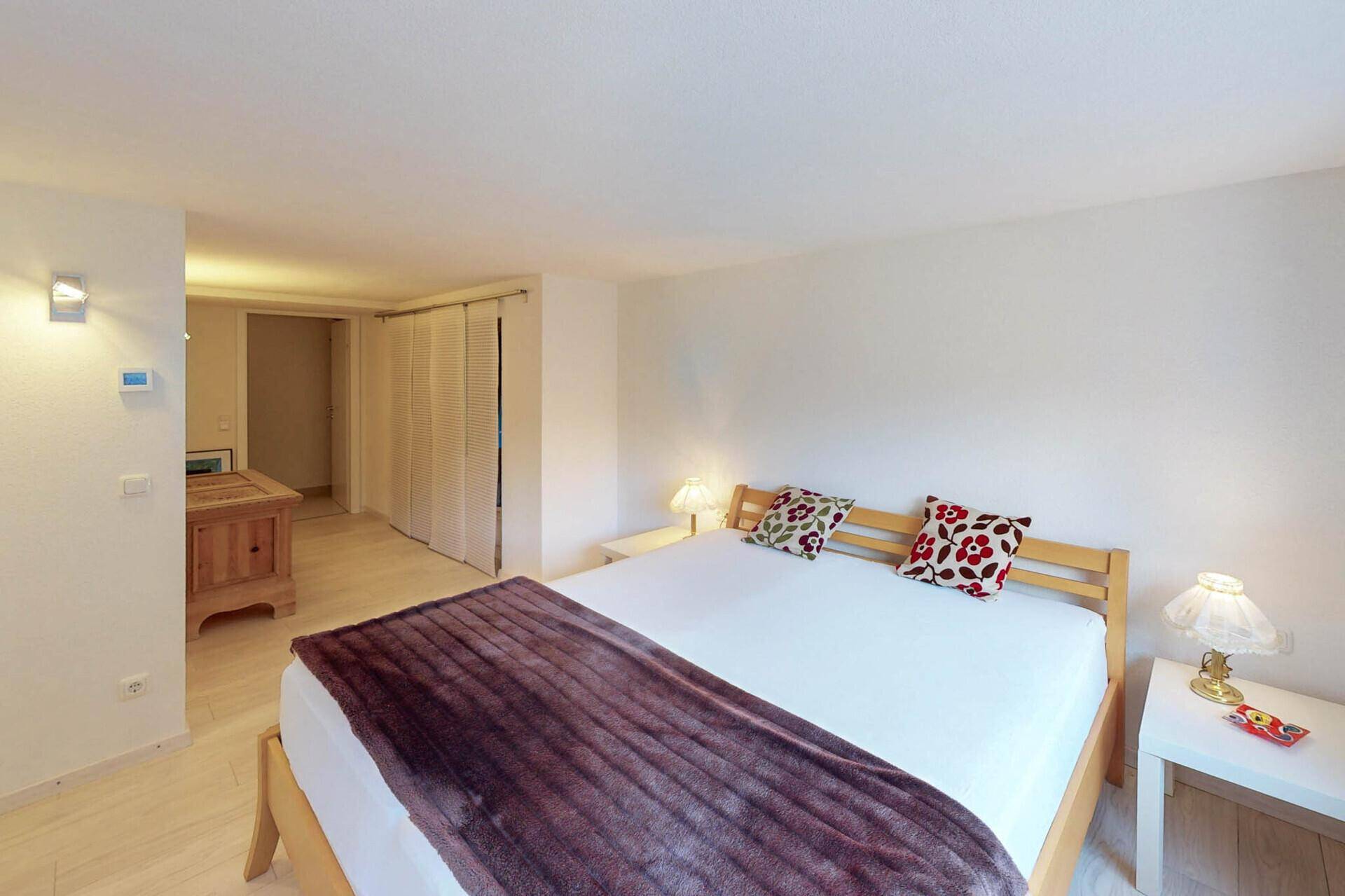 Helles Schlafzimmer mit Doppelbett, Parkettboden und Schiebetüren.