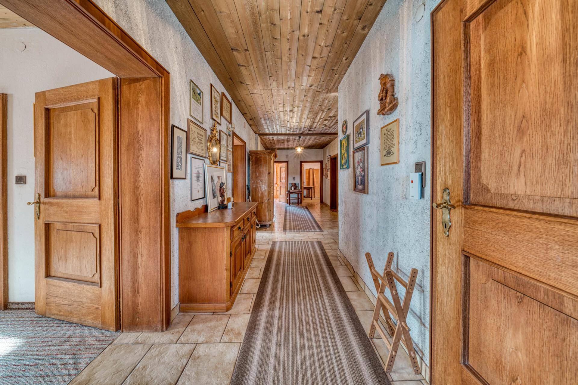 Langer Flur mit Holzdecke, Fliesenboden und traditionellen Holzmöbeln.