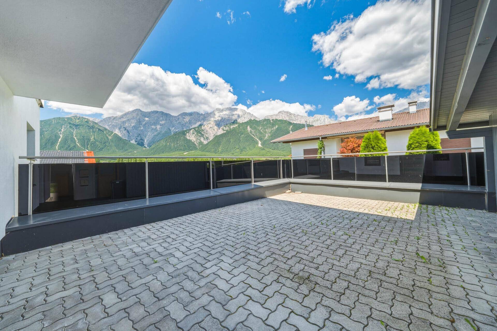 Großer gepflasterter Außenbereich mit Glasgeländer und weitem Bergblick.