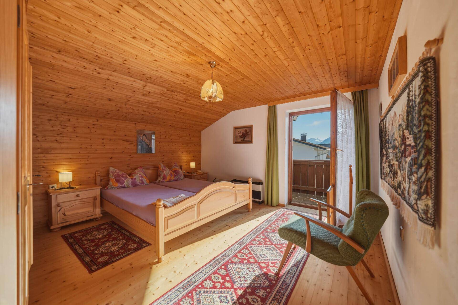 Schlafzimmer im Dachgeschoss mit Holzverkleidung, Doppelbett und Balkonzugang mit Bergblick.
