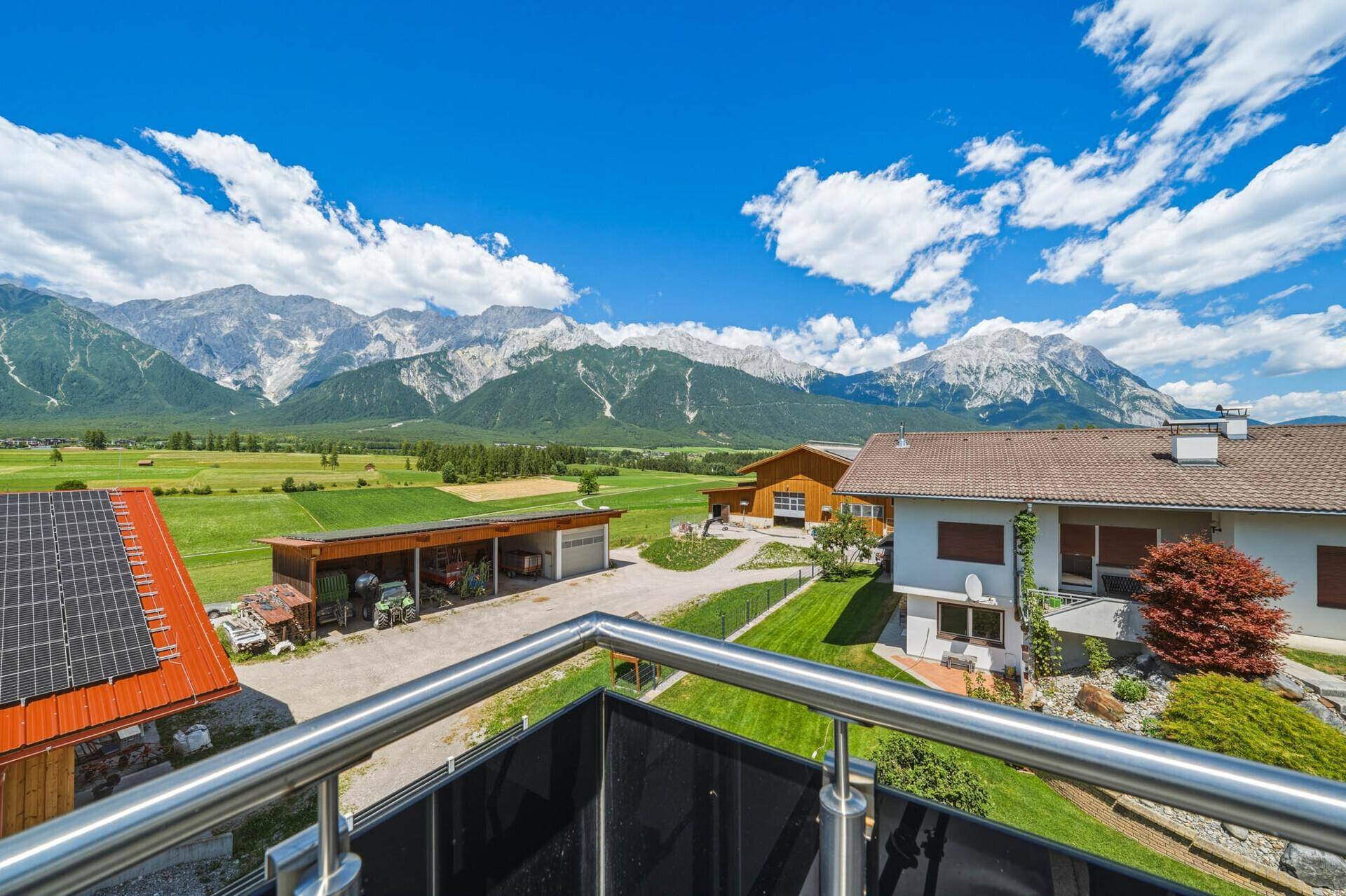 Panoramablick vom Balkon auf die majestätischen Berge und die grüne Landschaft unter blauem Himmel.