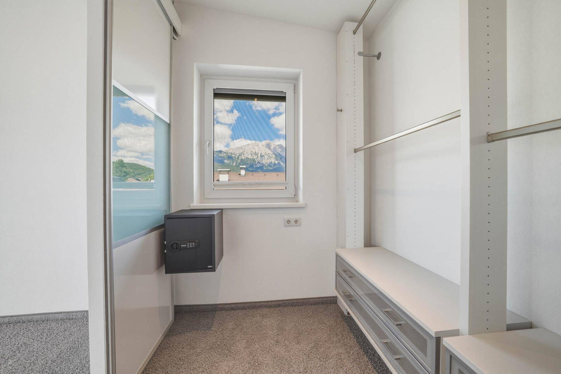 Heller begehbarer Kleiderschrank mit Fenster, Regalen und einem eingebauten Safe.