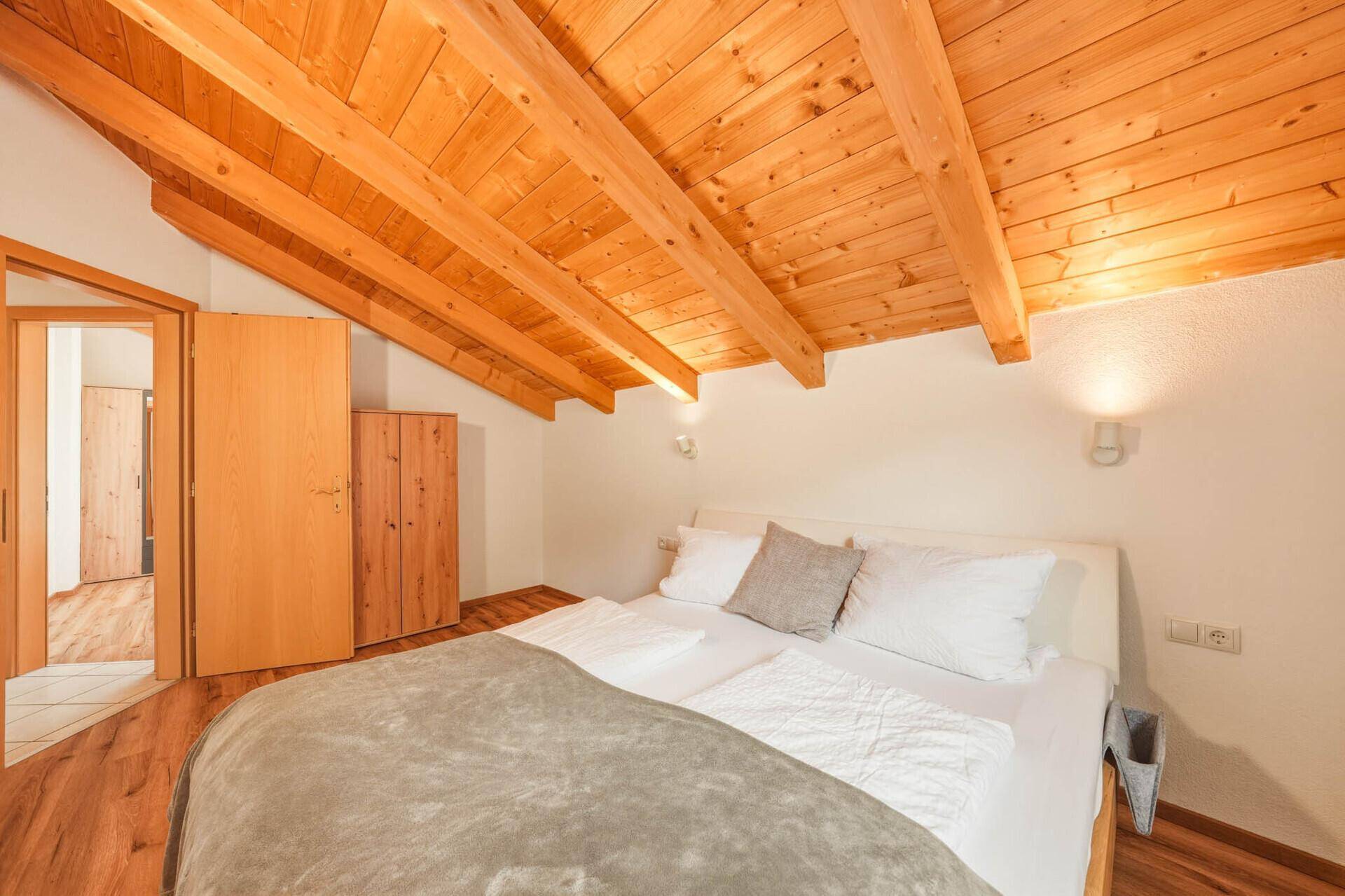 Schlafzimmer mit Holzbalkendecke, Holzboden und einem Kleiderschrank aus hellem Holz.