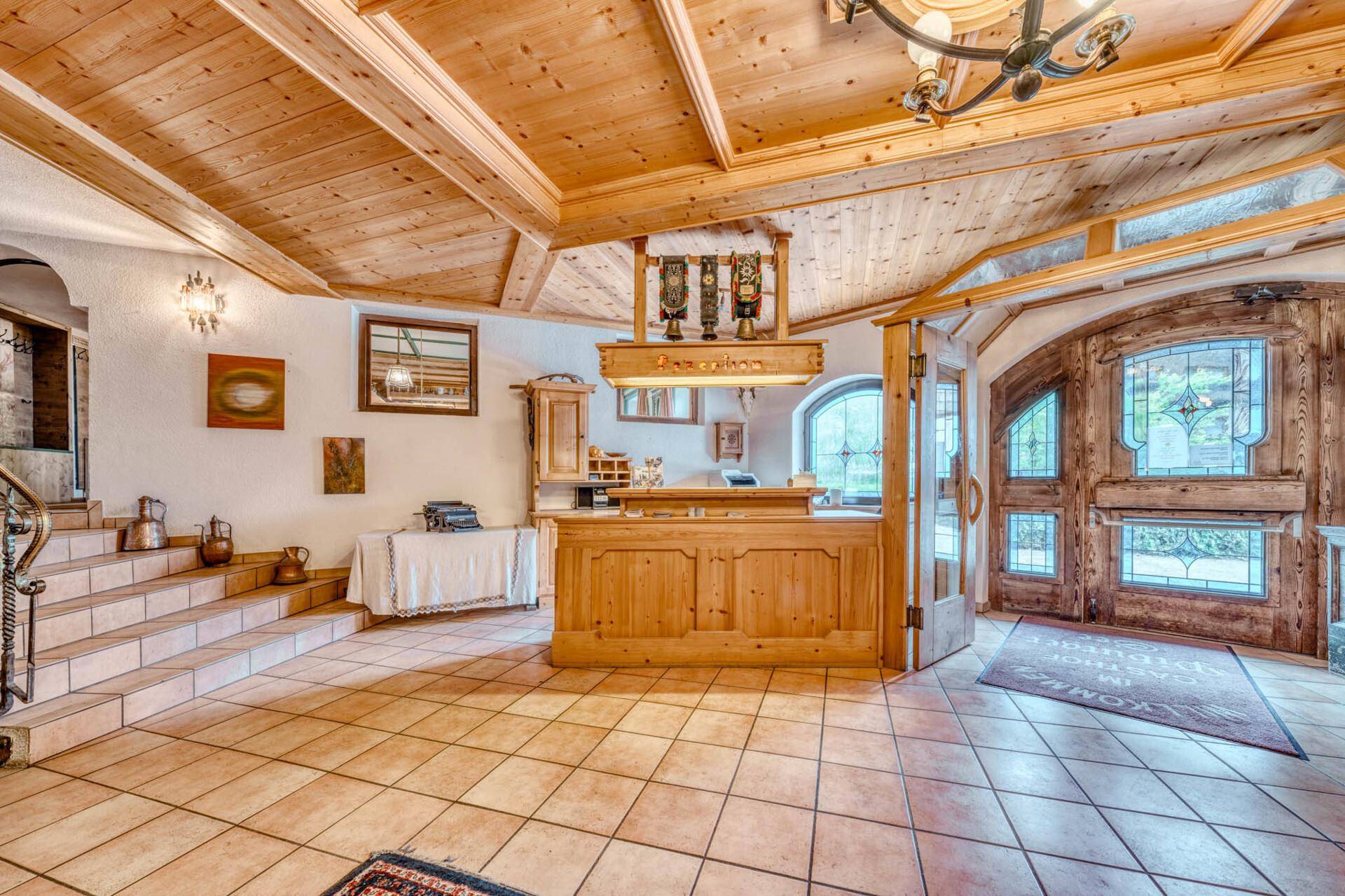 Empfangsbereich im alpinen Stil mit Holzvertäfelung, Fliesenboden und einer rustikalen Rezeption.
