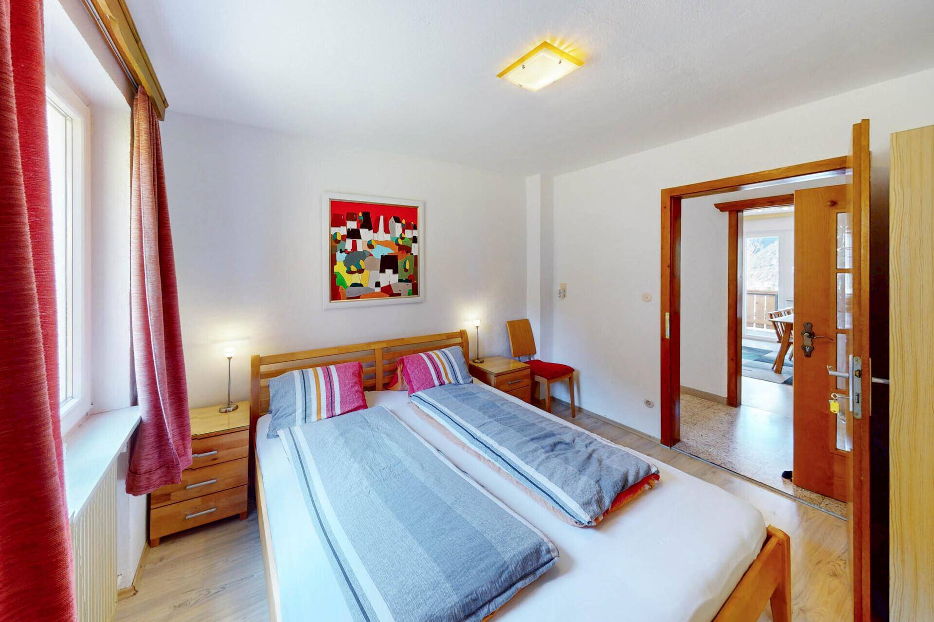 Helles Schlafzimmer mit Doppelbett, Fenster und Blick auf die Berge.