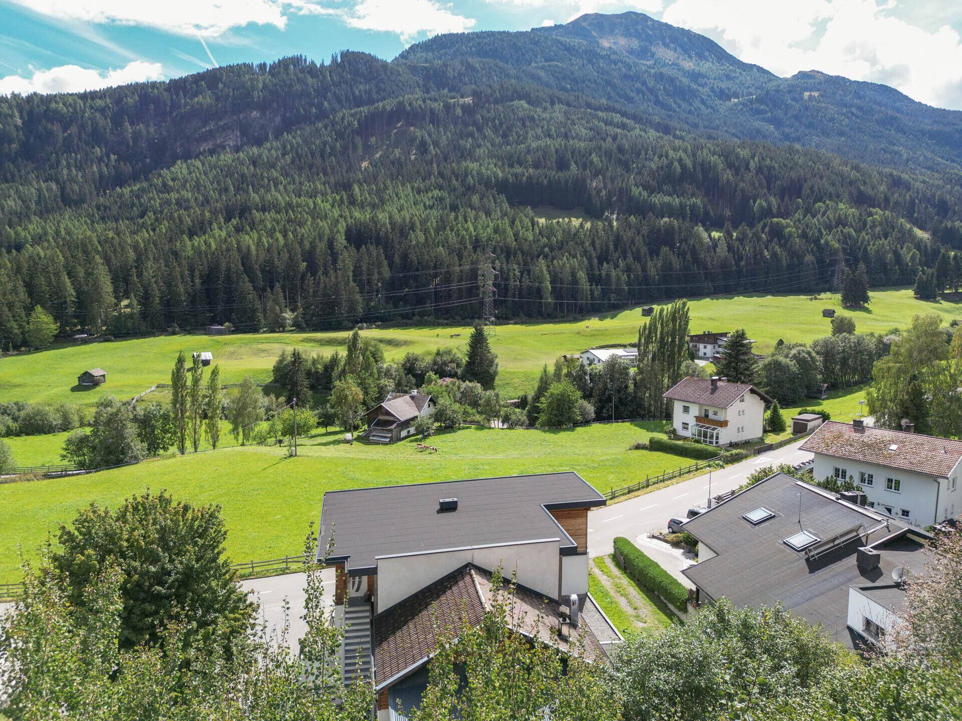 Aussicht auf moderne Häuser mit Flachdächern, eine Straße und die umliegende grüne Berglandschaft.