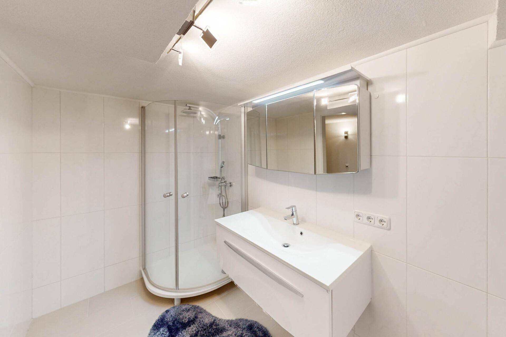 Helles Badezimmer mit Duschkabine, Waschbecken und Spiegelschrank.