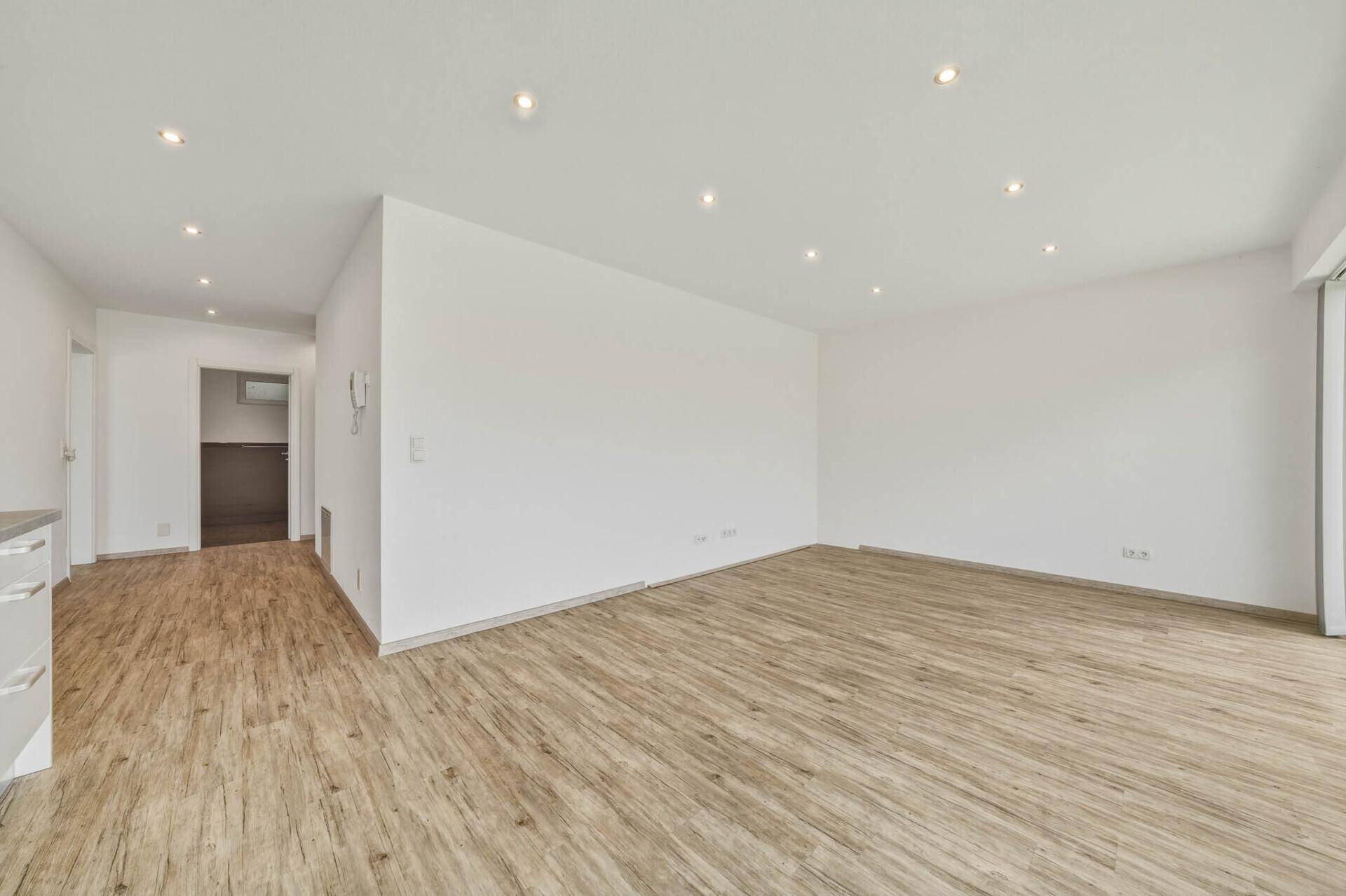 Geräumiger Wohnbereich mit hellem Laminatboden und weiß gestrichenen Wänden, bereit zur individuellen Gestaltung.